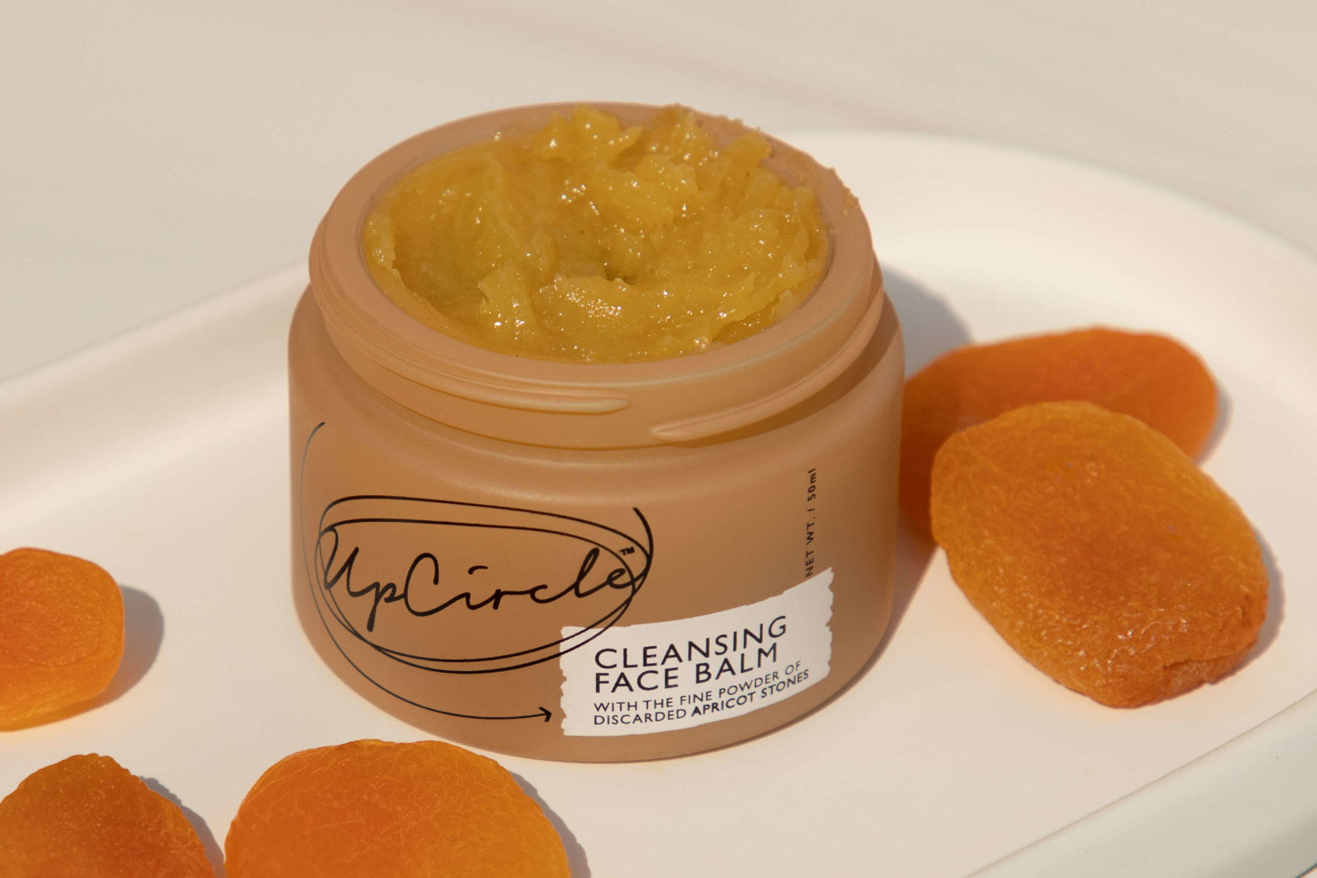 Tub of skin cream surrounding by apricots