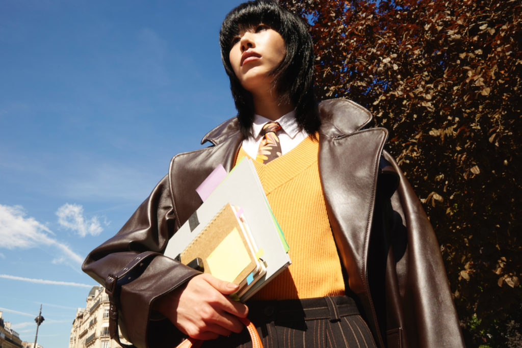 Model in brown leather jacket holding papers and books