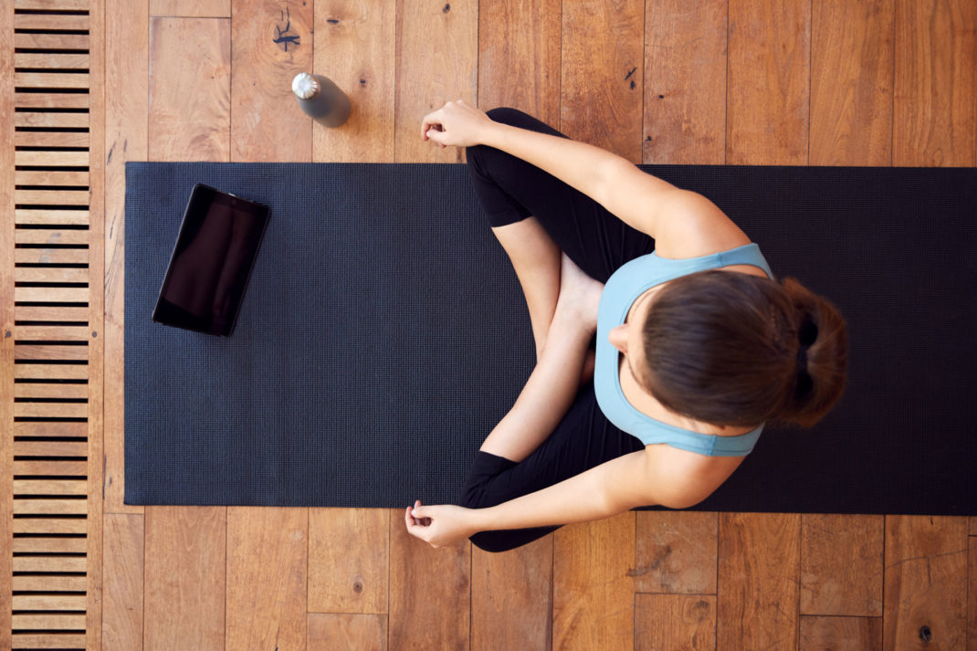 an overhead shot of a yogi meditating on a harwood floor, with a tablet next to her