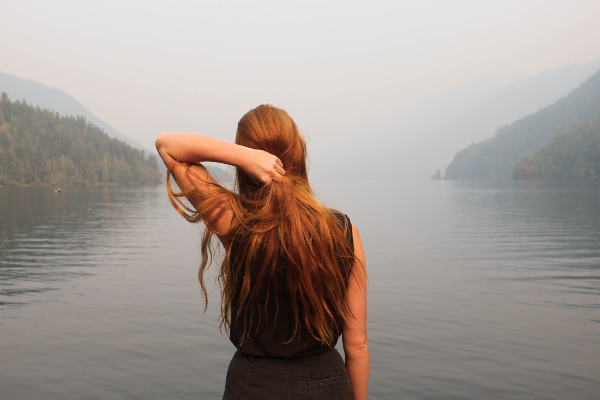 Woman with red hair looking out at misty lake