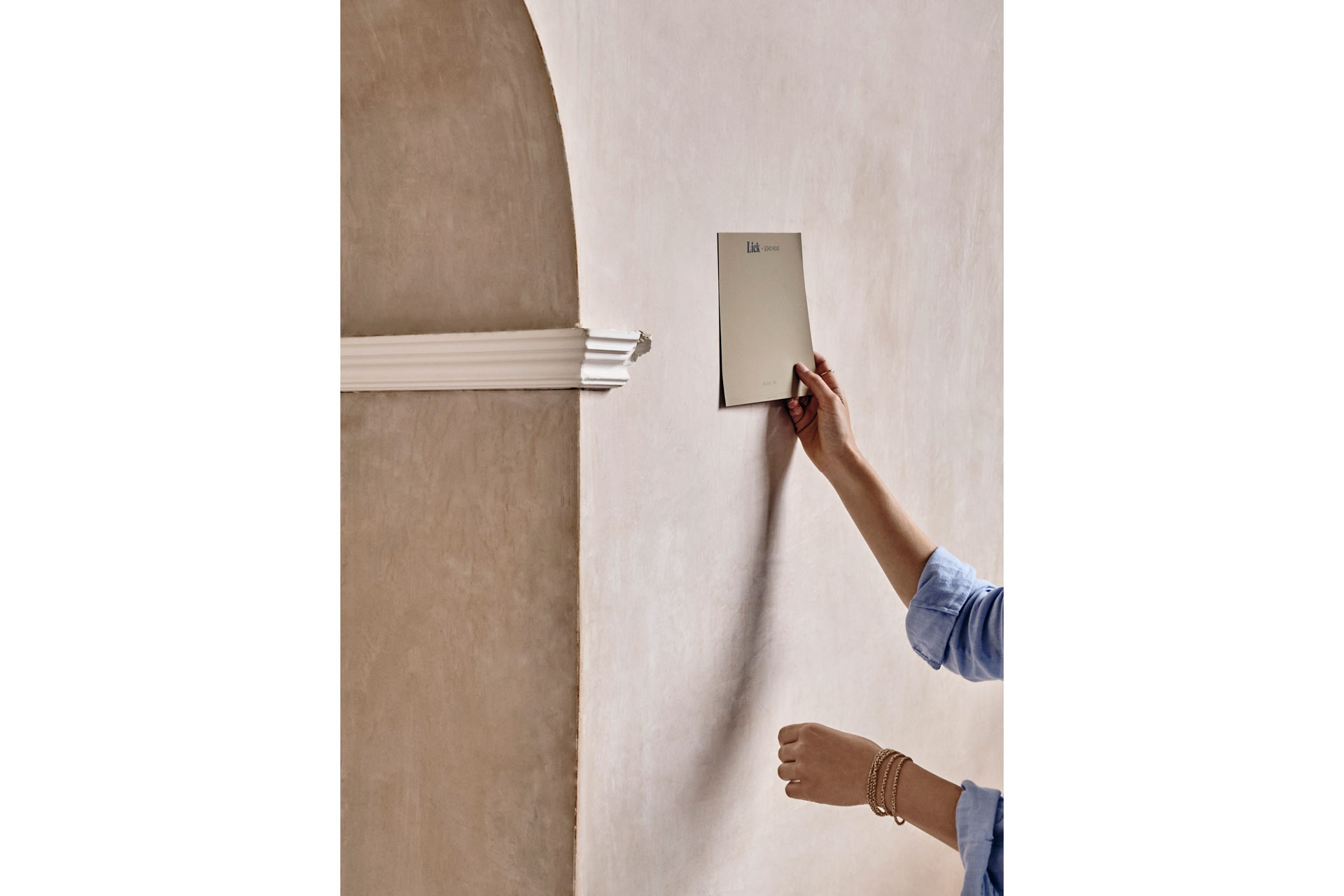 Lick x Soho House have a new paint collaboration. This image is of a woman holding up a cream swatch to a cream, historic wall
