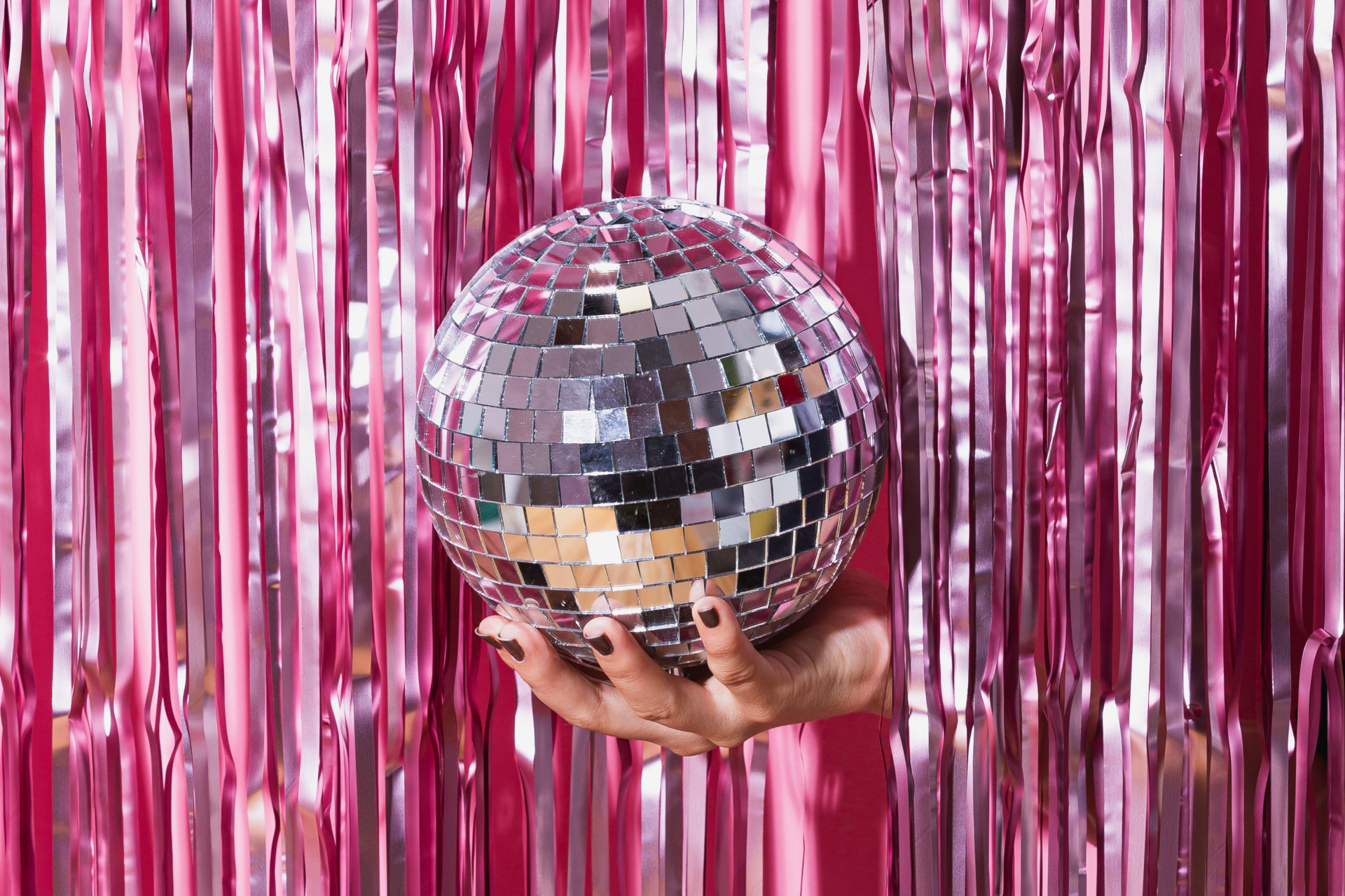 Hand holding a disco ball through pink streamer curtain