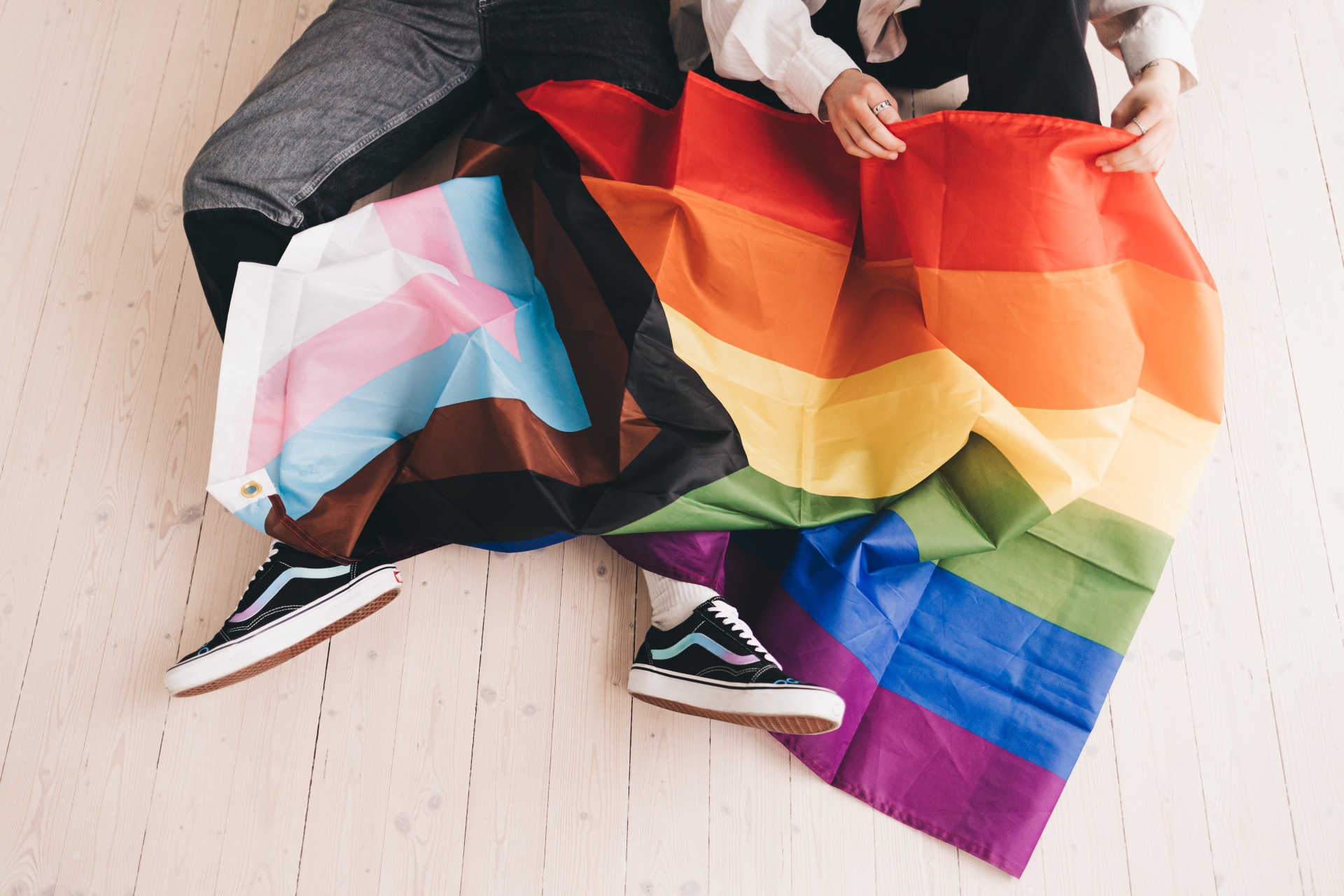 Two people sat on the floor with pride flags on their legs