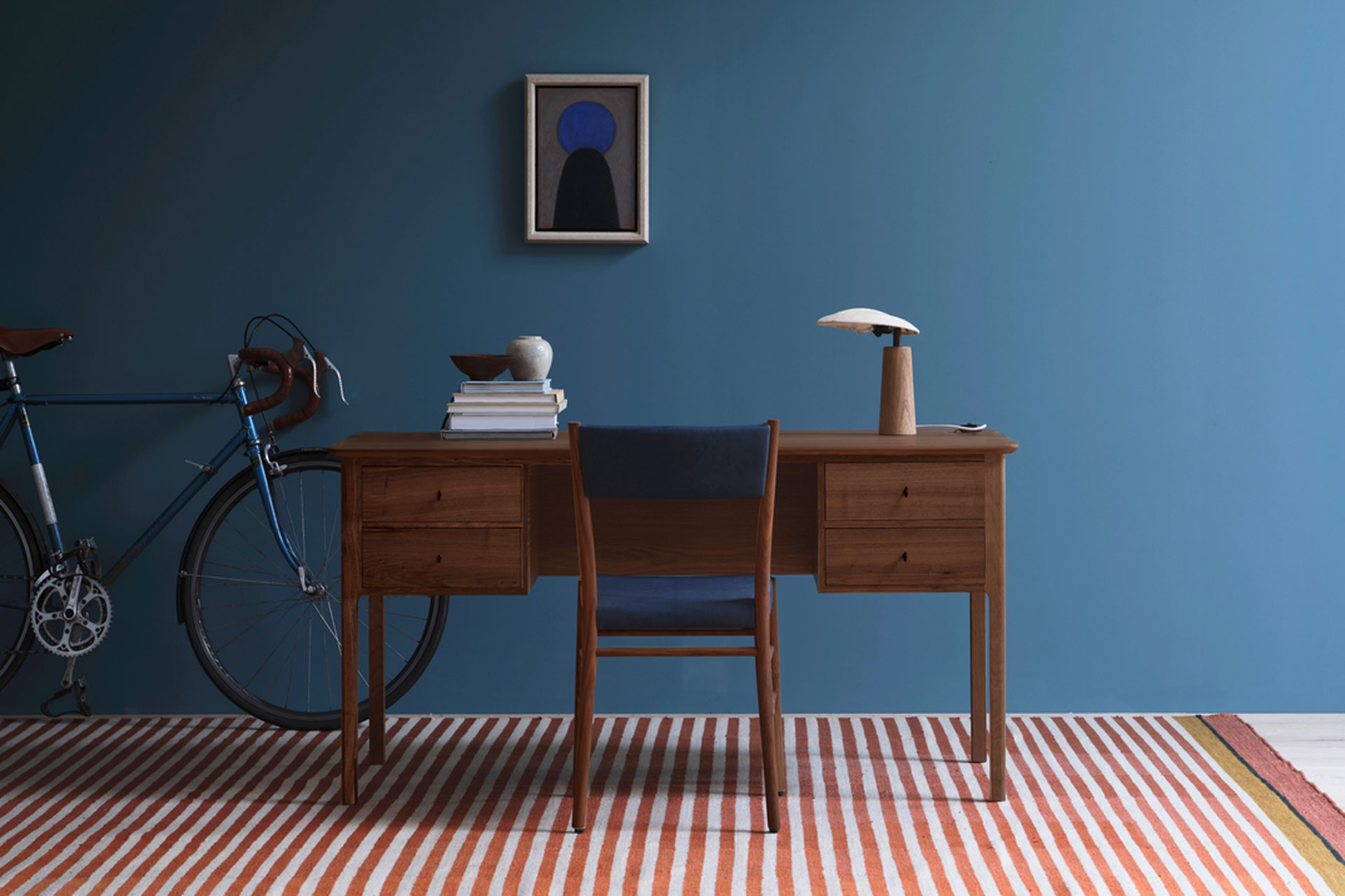 Doyle desk Pinch, in a blue walled living room with a stripey rug and bike