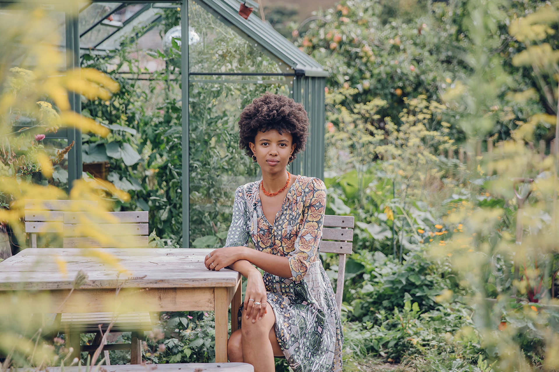 Poppy Okotcha in a garden with a greenhouse behind it