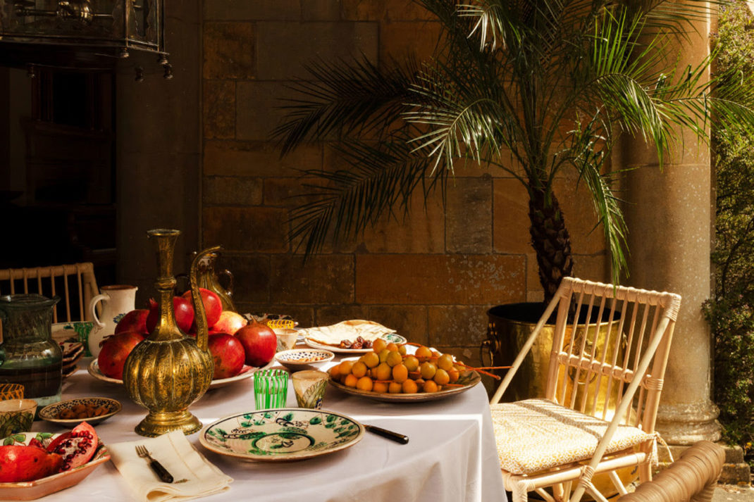 a scene of a Egypt rattan chair, fruits and an elaborate golden jug, with a palm tree behind