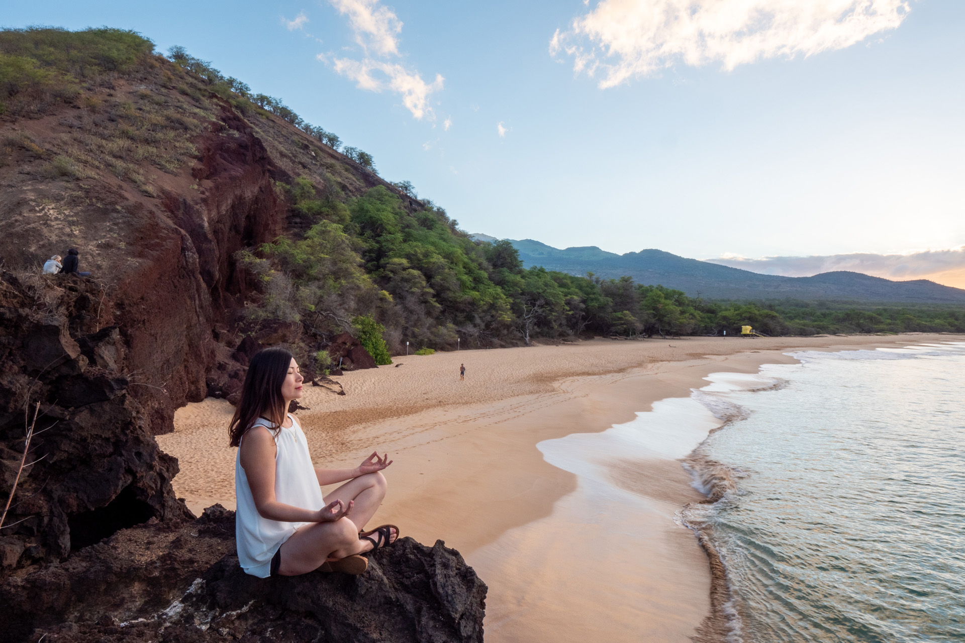 a woman meditates on a beach with the sea stretching into the distance