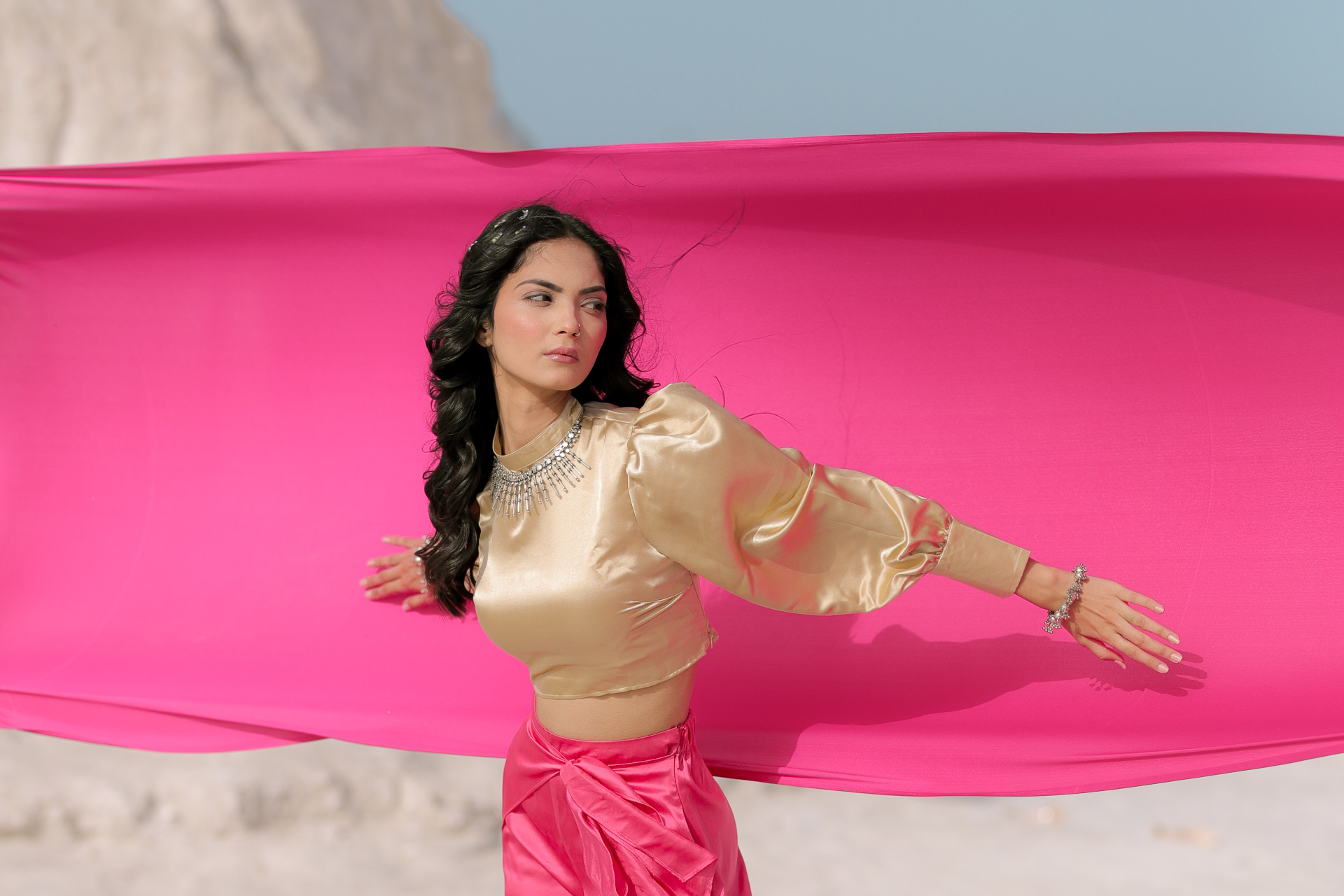 Model in silk crop top and bottoms stood in front of pink fabric