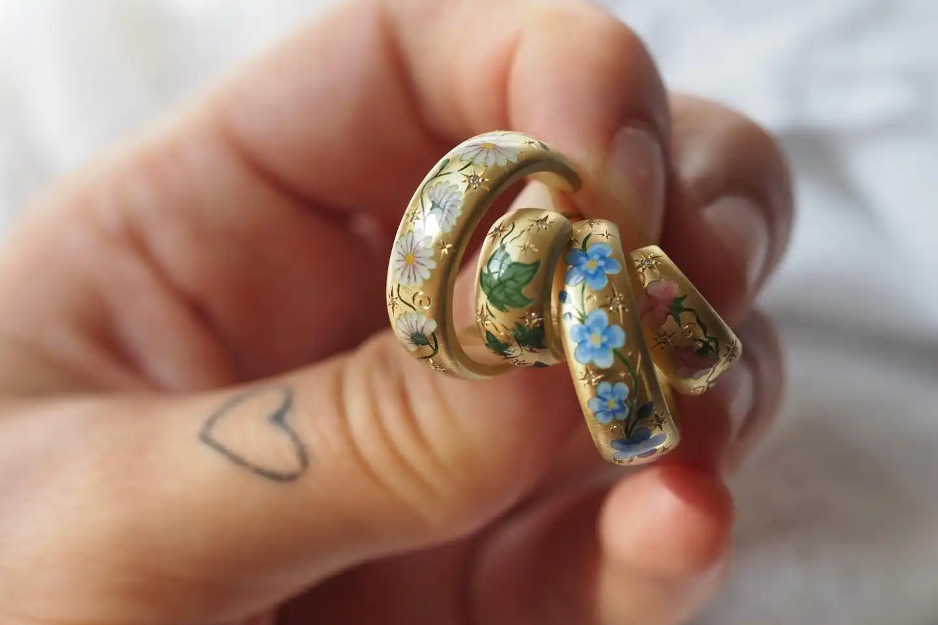 Hand holding gold earrings painted with flowers