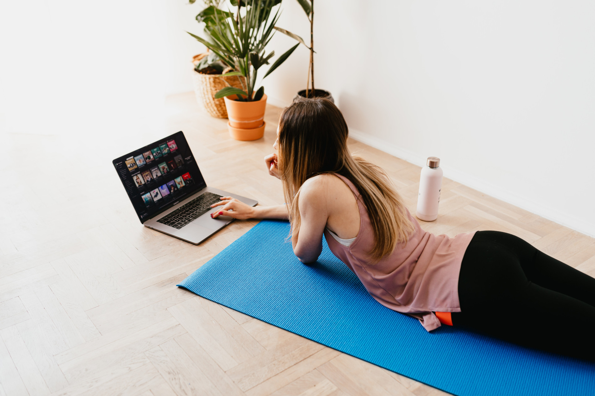 Woman lying on exercise mat while on her laptop