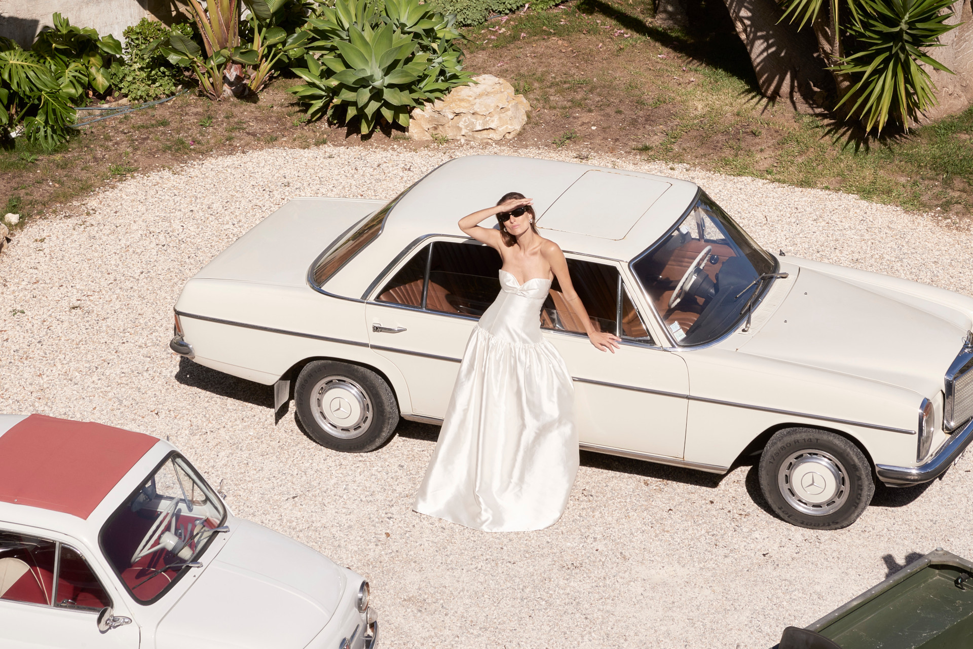 Model in wedding dress stood by white vintage car