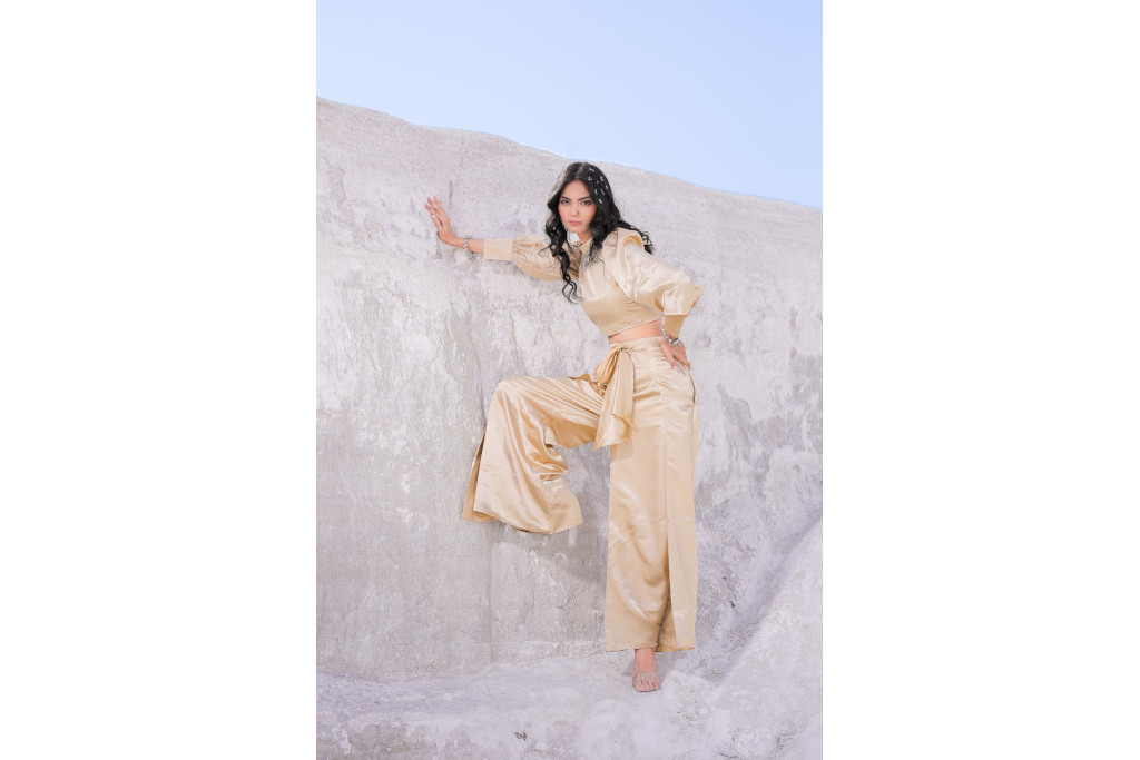 Model in champagne coloured silky top and trousers leaning against a stone wall