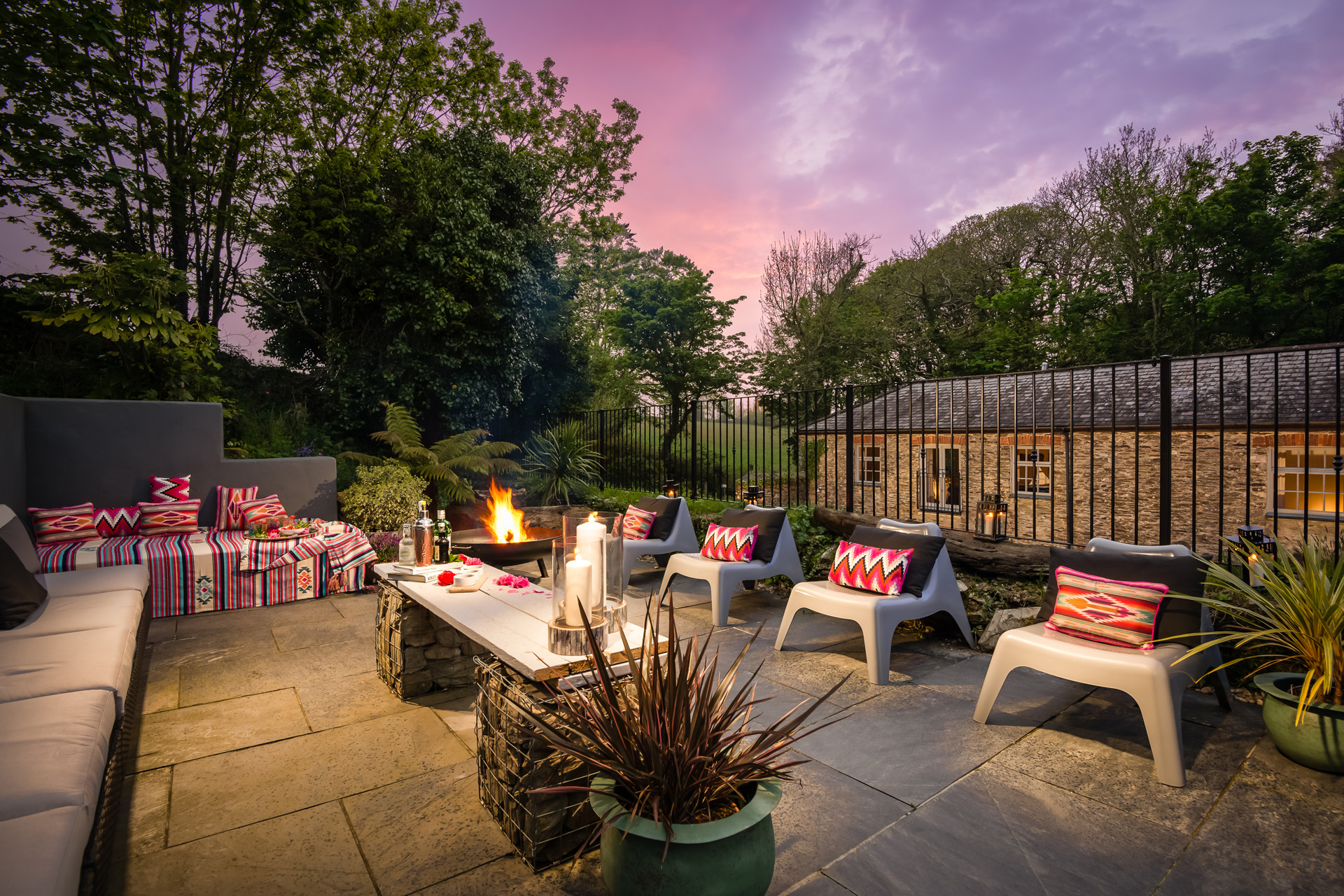 the back yard at The Willows at dusk, with chairs and cushions gathered around a fire