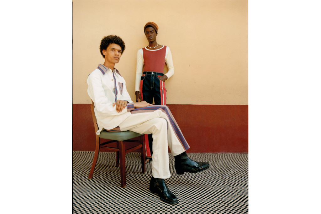 Two black models, one sat on a chair and the other stood, in a neautral colour room with pattern carpets