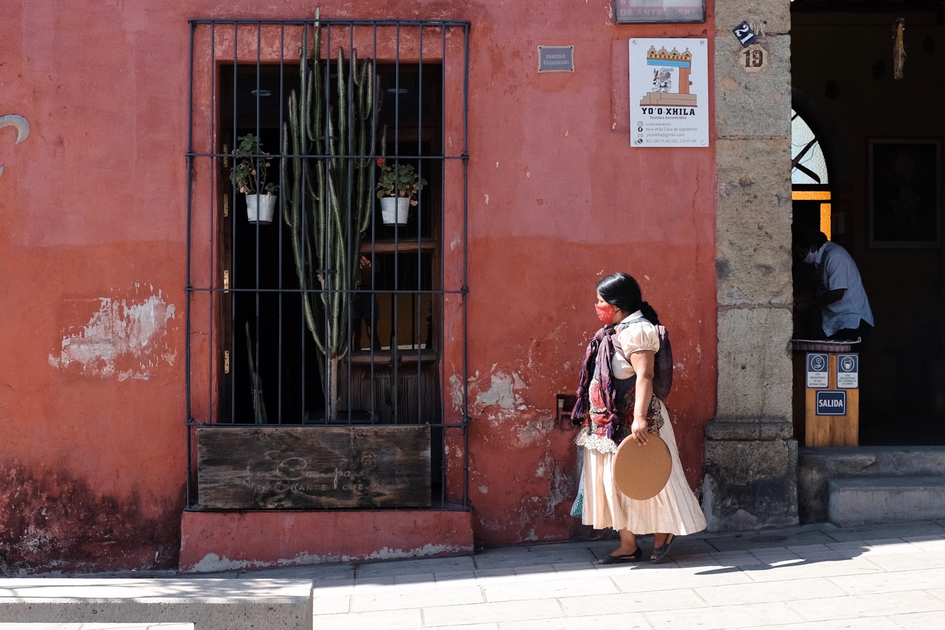 a woman stood by a red building with a cactus