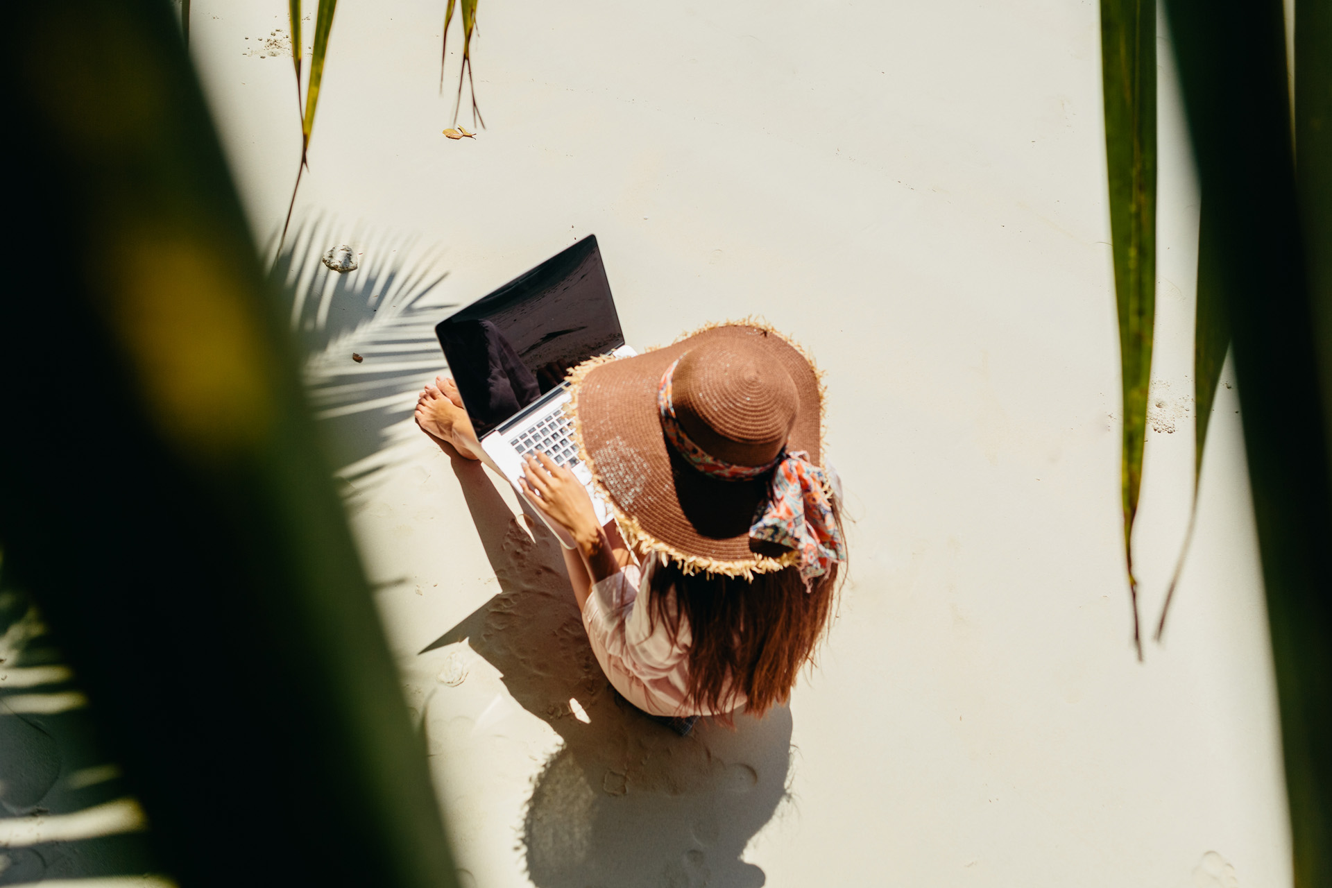 Woman freelancer on the beach. Working remotely on the laptop computer through the internet. Working while travelling. Top view.