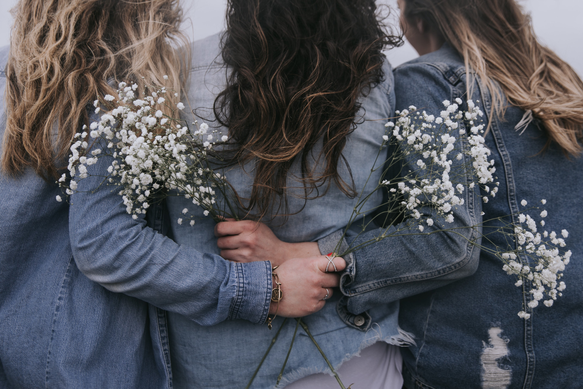 Close up of three women's backs, wearing denim jackets and holding flowers