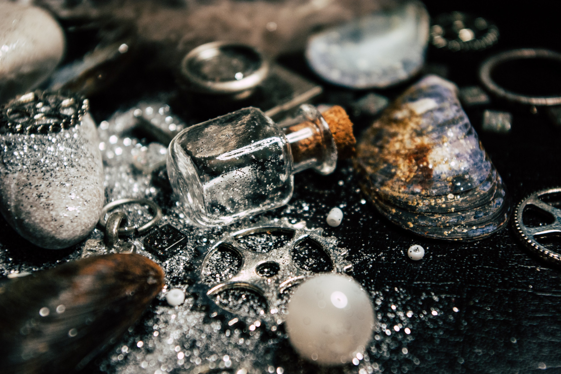 Vials of glitter, pearls and silver cogs on black fabric