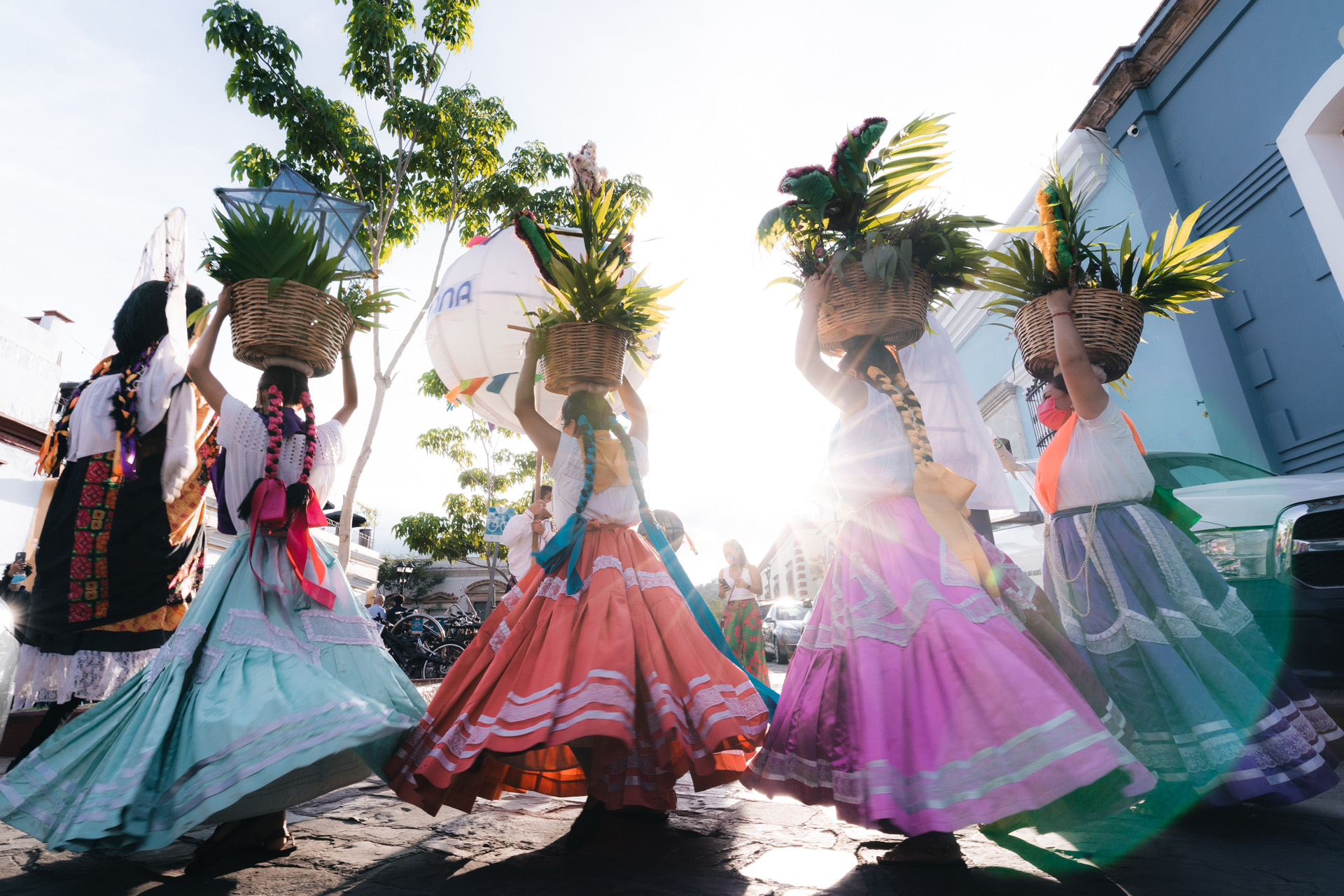 girls with long plaited hair and colourful skirts carrying baskets of leaves