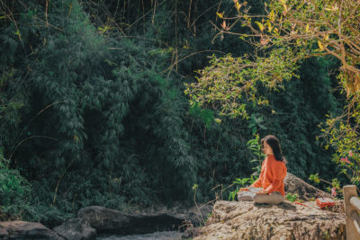 a woman meditating on a rock surrounded by trees