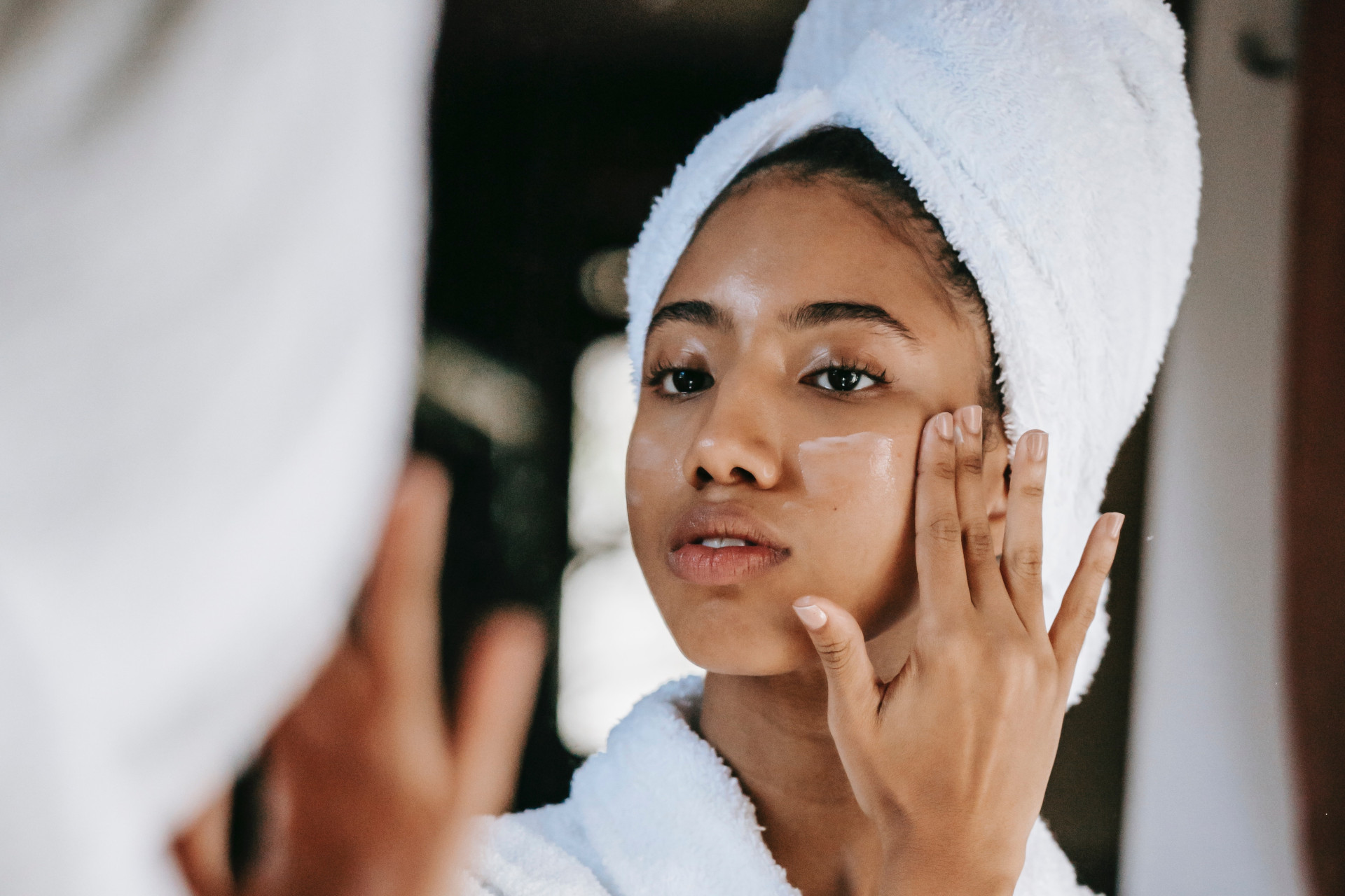 Close up of black woman with hair in a white towel applying face cream