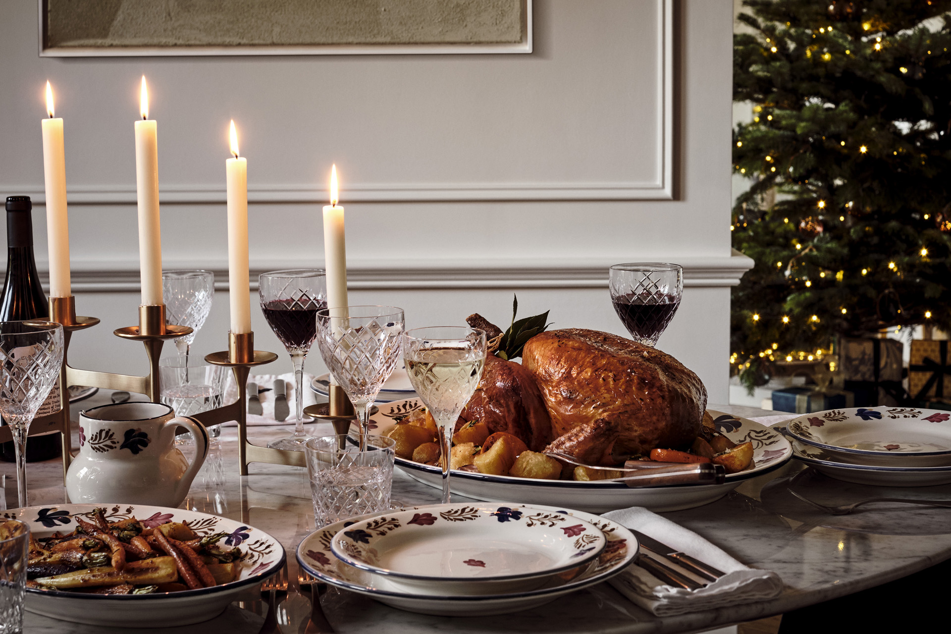 a festive table with turkey, candles, plates and a christmas tree
