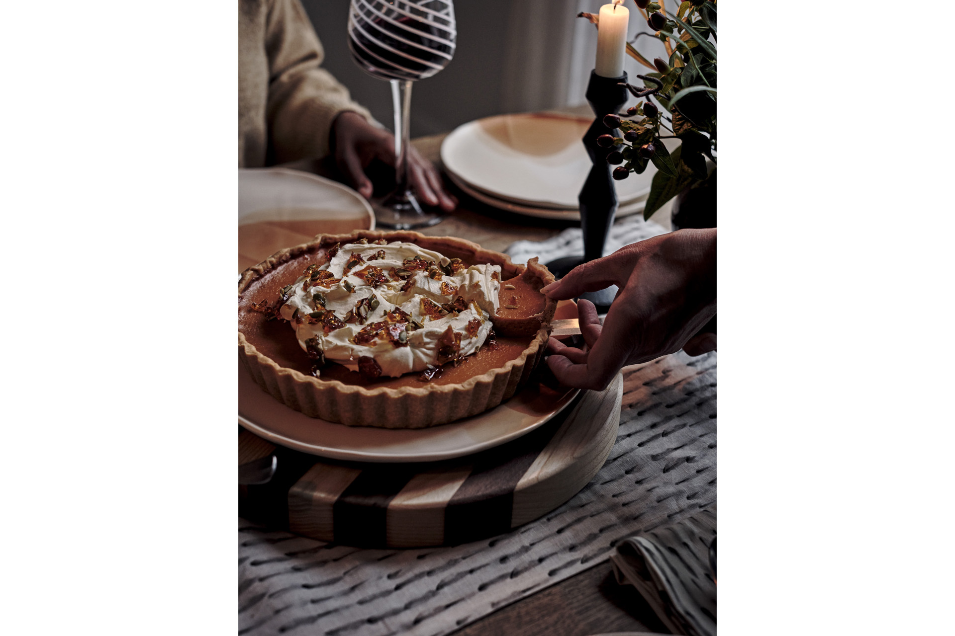 someone cutting a slice from a pumpkin pie with wine glass and candle