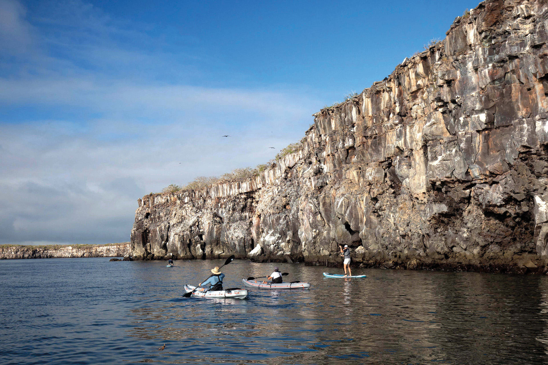 people kayaking in front of a cliff face