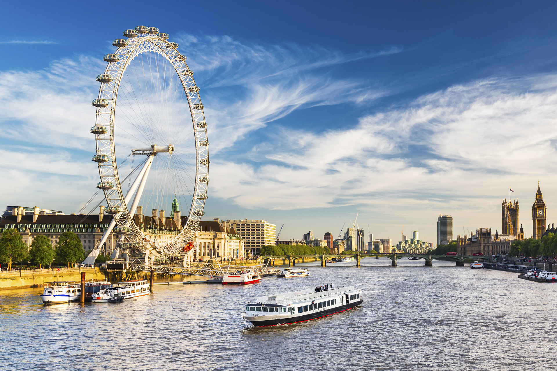 View of Westminster Parliament, Big Ben and London Eye with Thames and tourist ship in foreground on a sunny summer afternoon