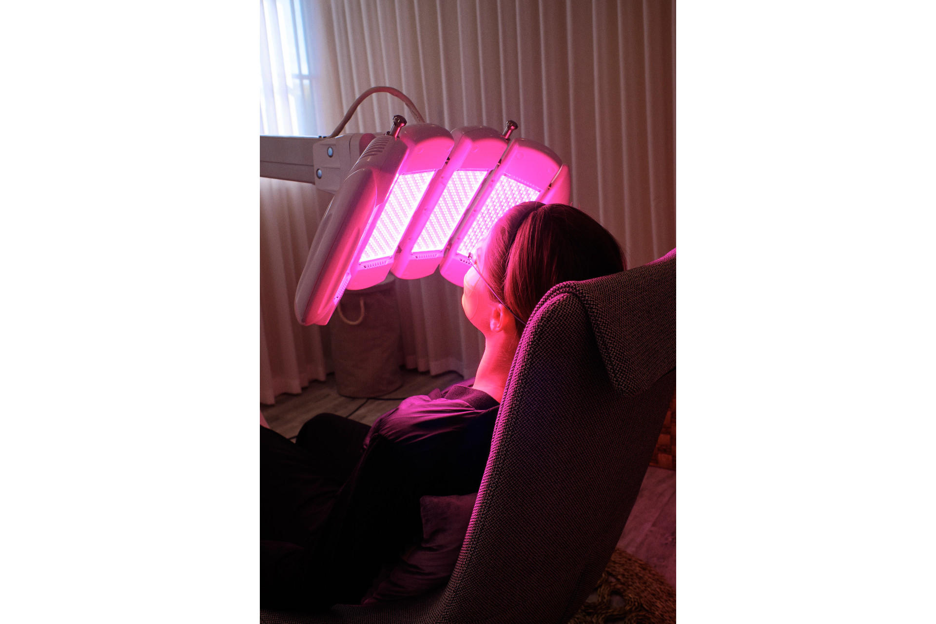 Woman sat in chair receiving LED treatment from pink light