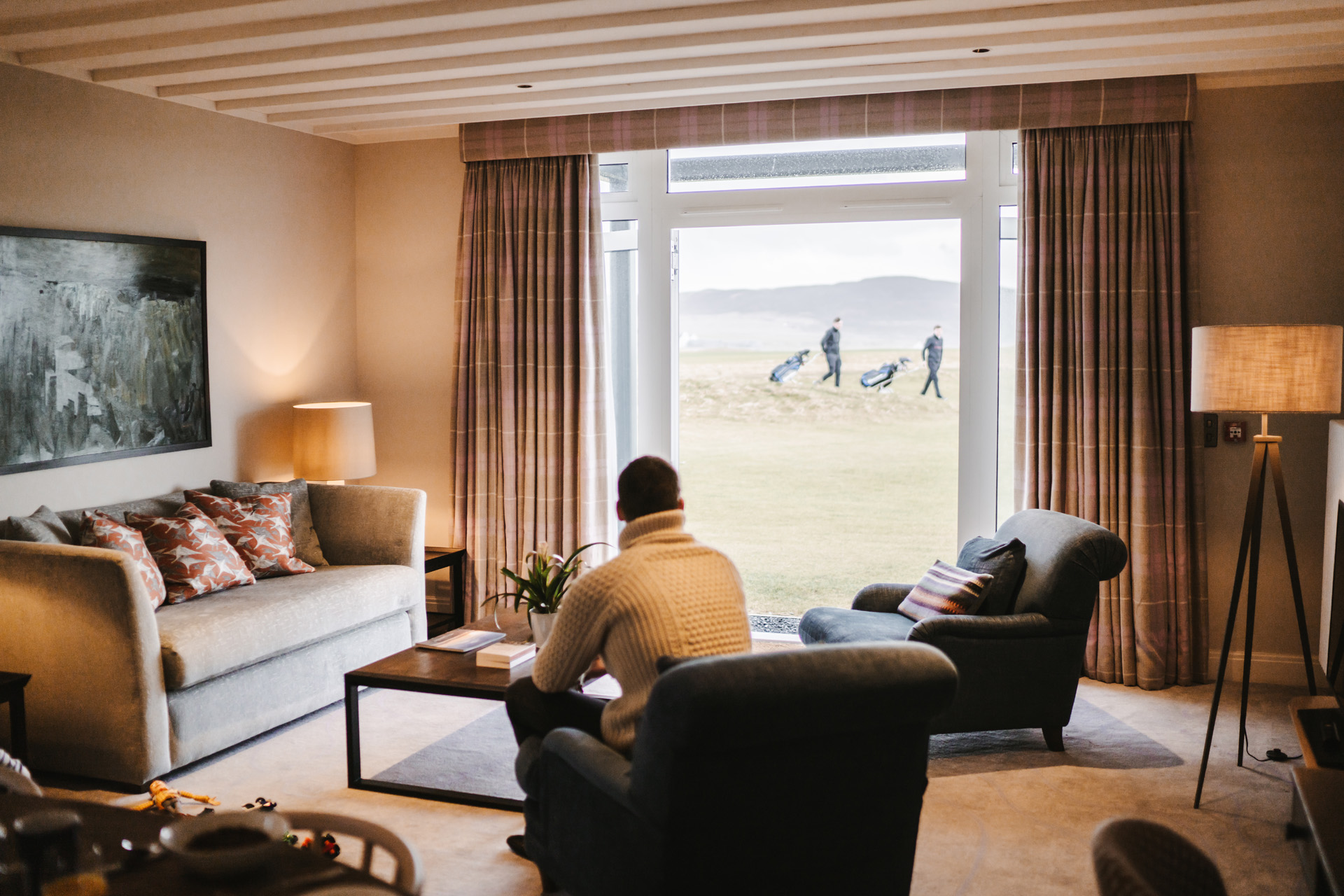 A man sat in a sitting room with patio doors and golfers