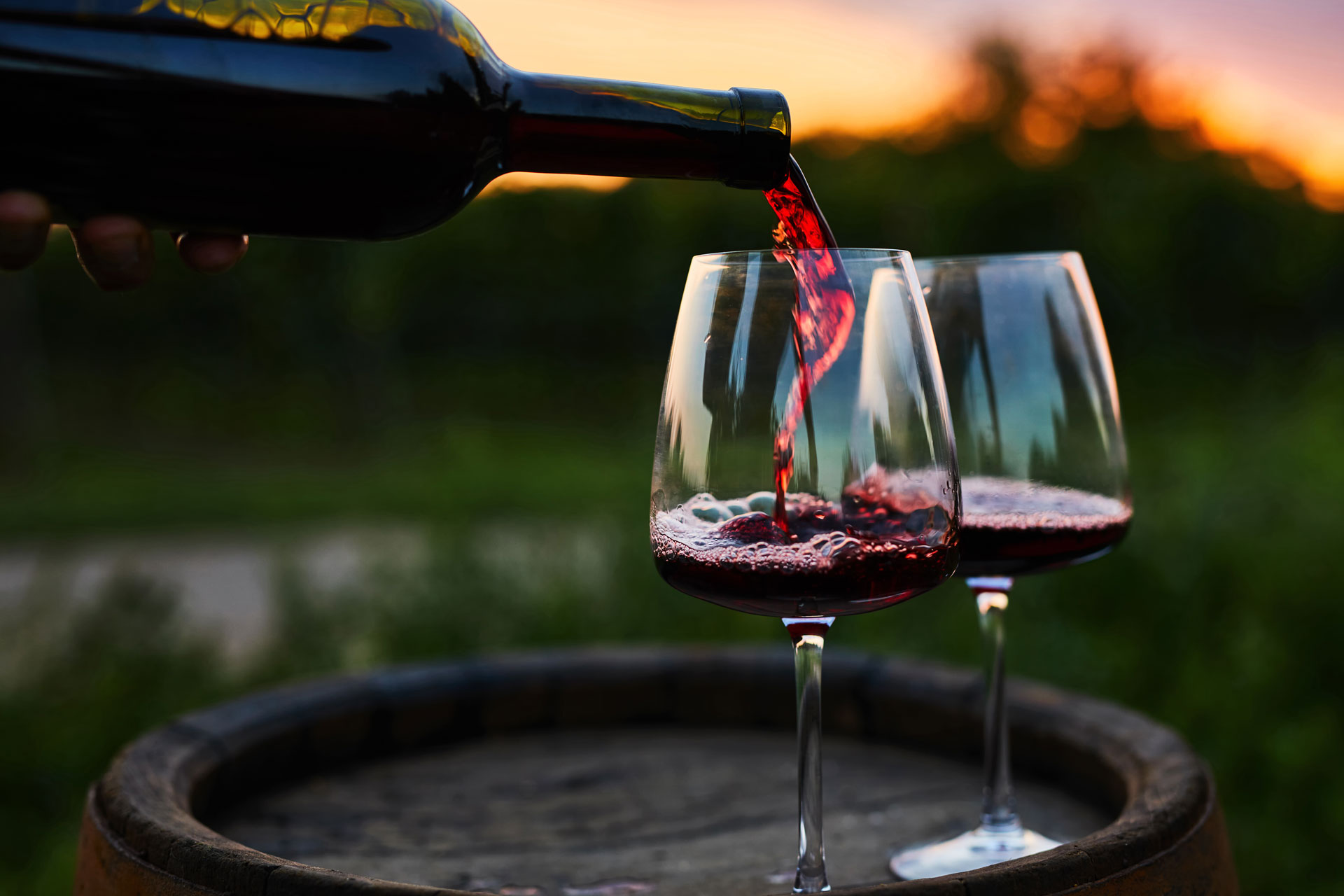 Pouring red wine into glasses on the barrel - stock photo