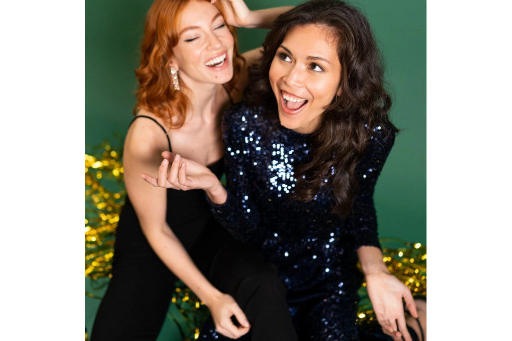 Two women sat together on green and gold background
