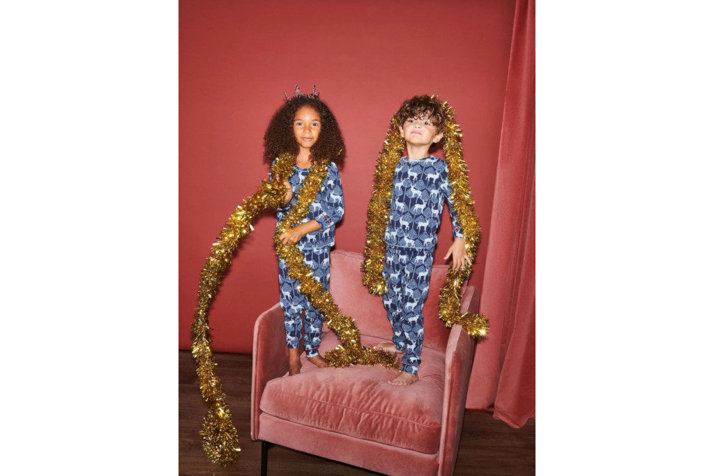 Two children in blue pyjamas stood on pink armchair with gold tinsel