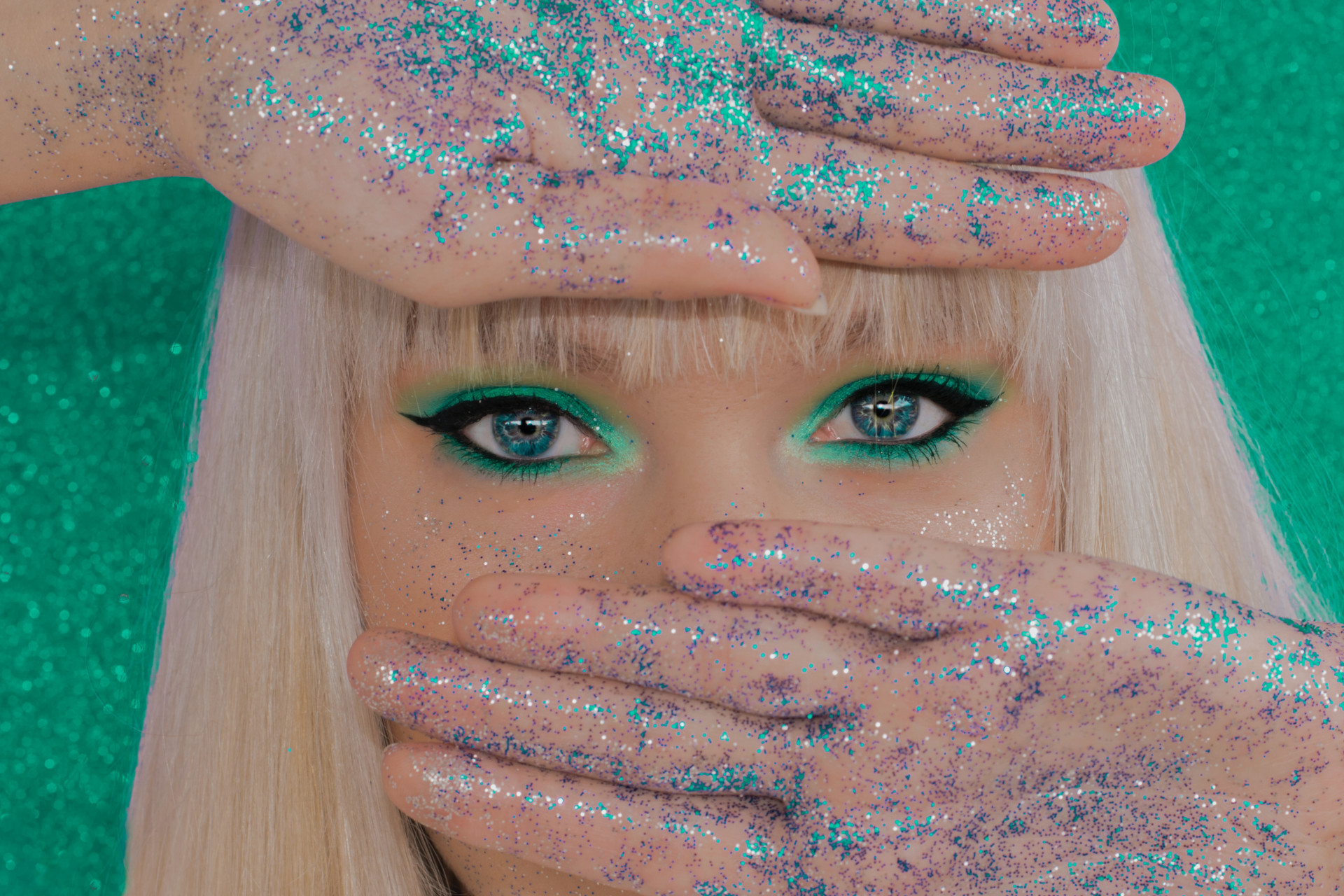 Woman covering part of her face, her hands covered in glitter