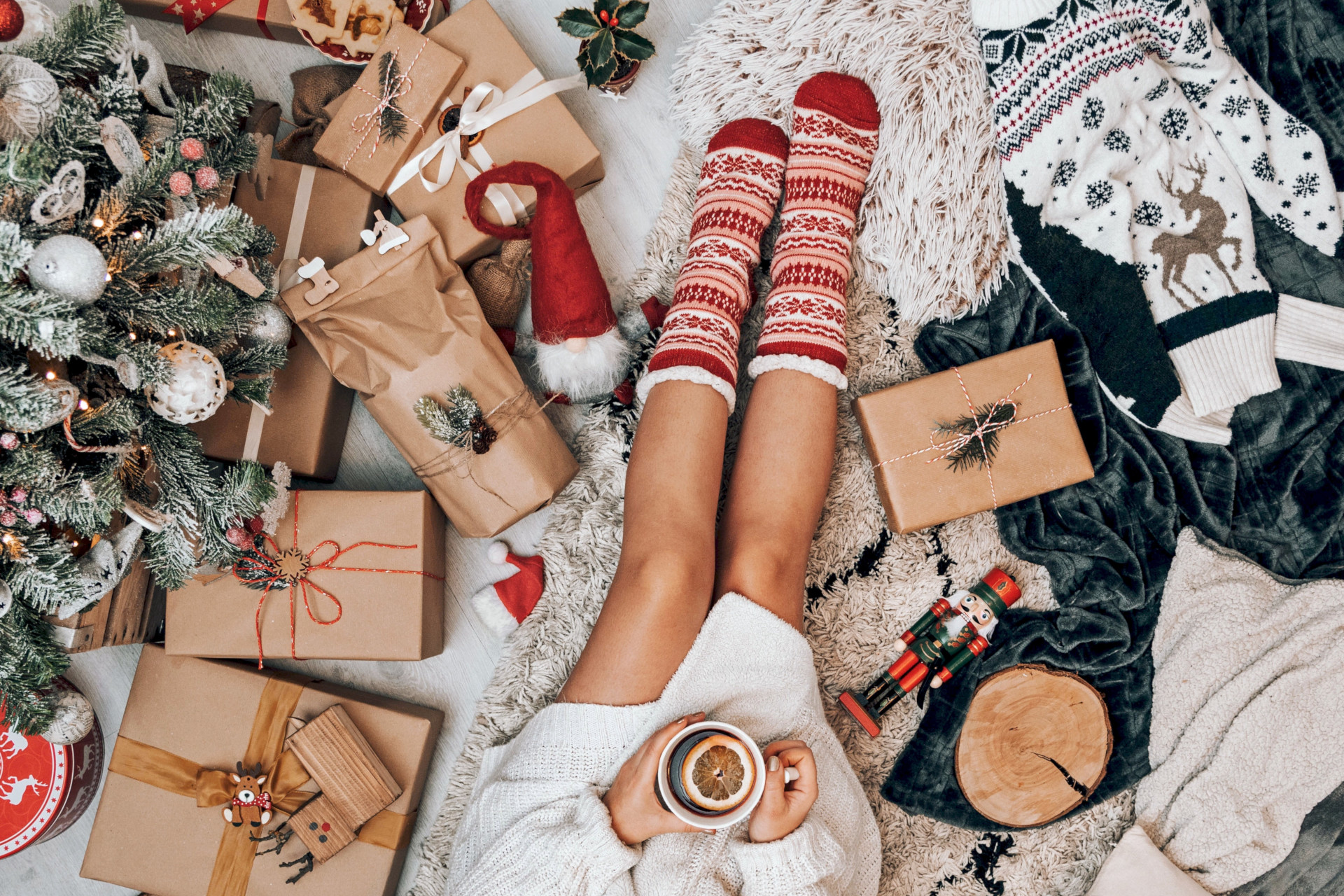 Overhead view of woman's legs in red fluffy socks, surrund by presents and Christmas tree