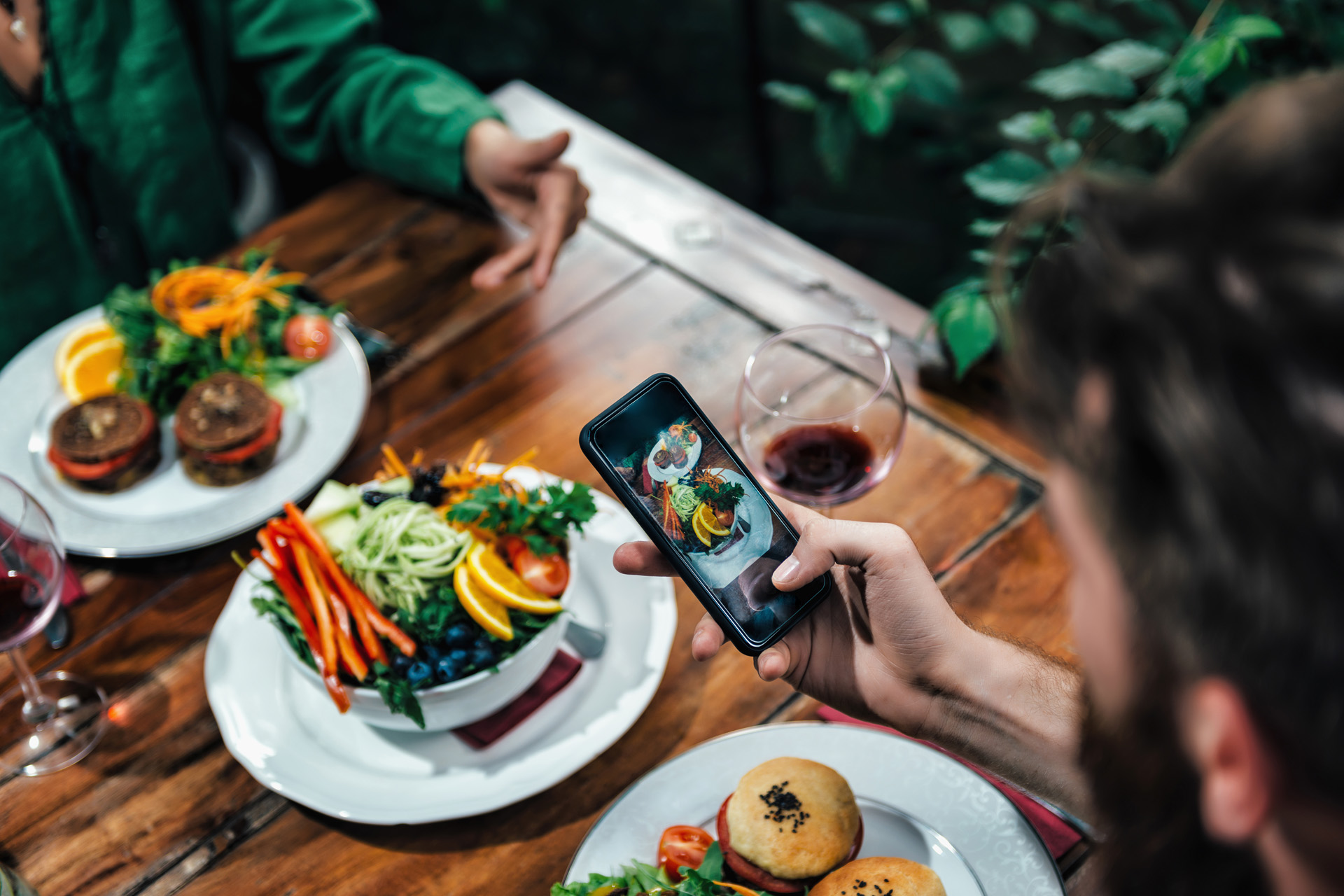 young couple photographing delicious vegetarian burger and mixed organic salad on white plate in vegetarian restaurant.