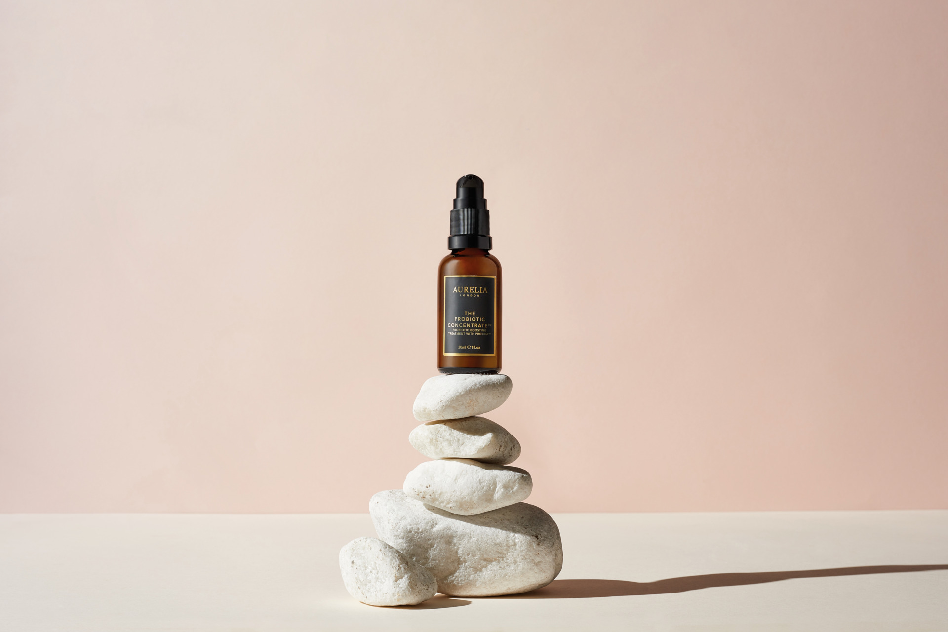 Brown and black bottle set on pile of stones on light pink background