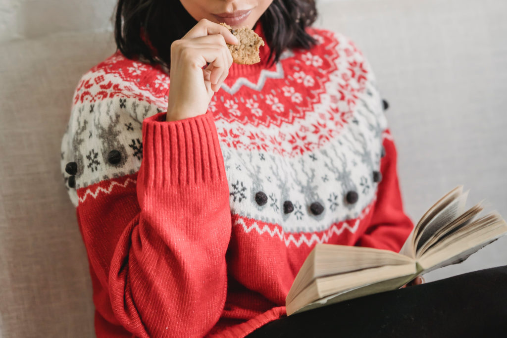 Woman in red Christmas jumper reading a book and eating a cookie
