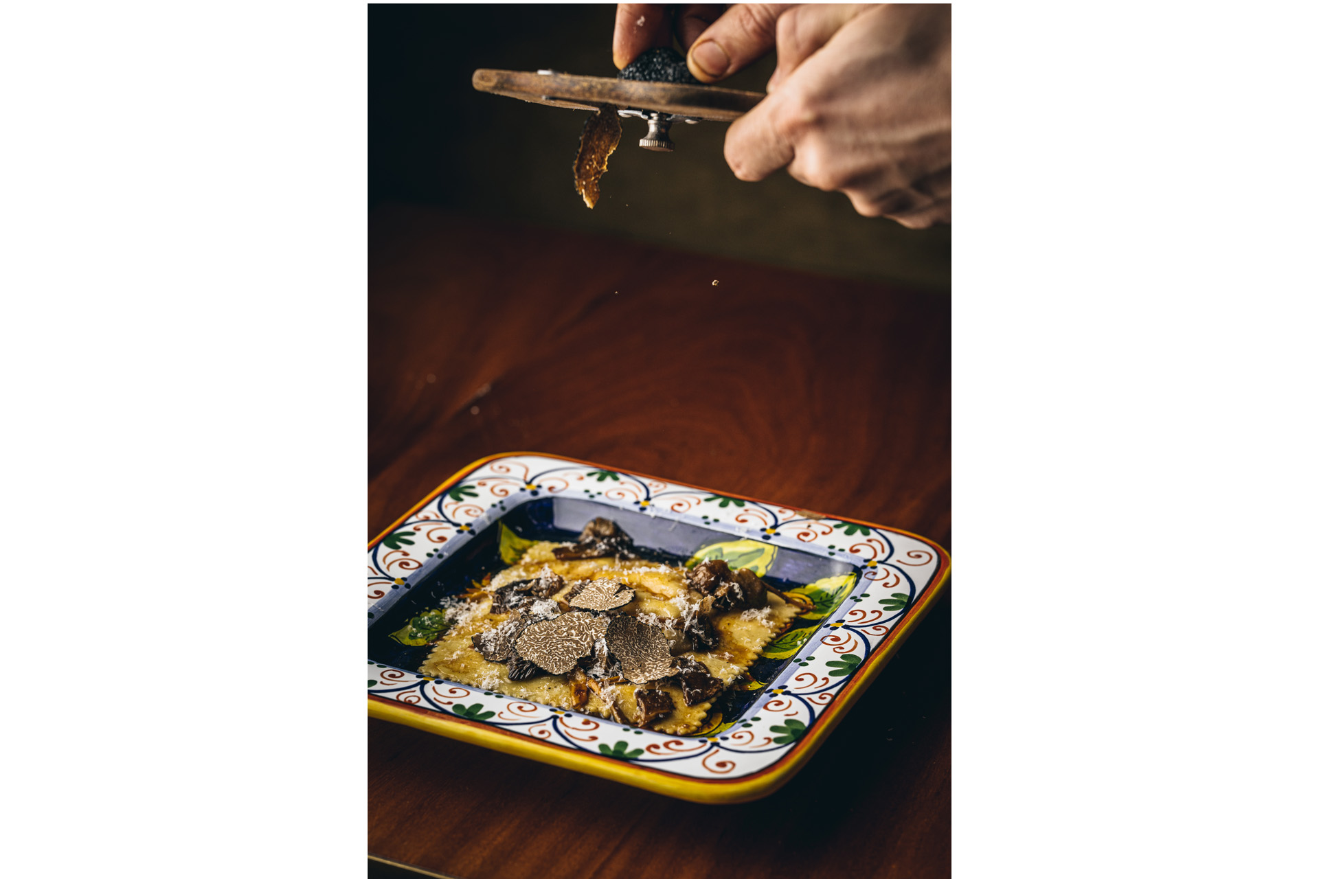 truffle being shaved over a bowl of raviolo