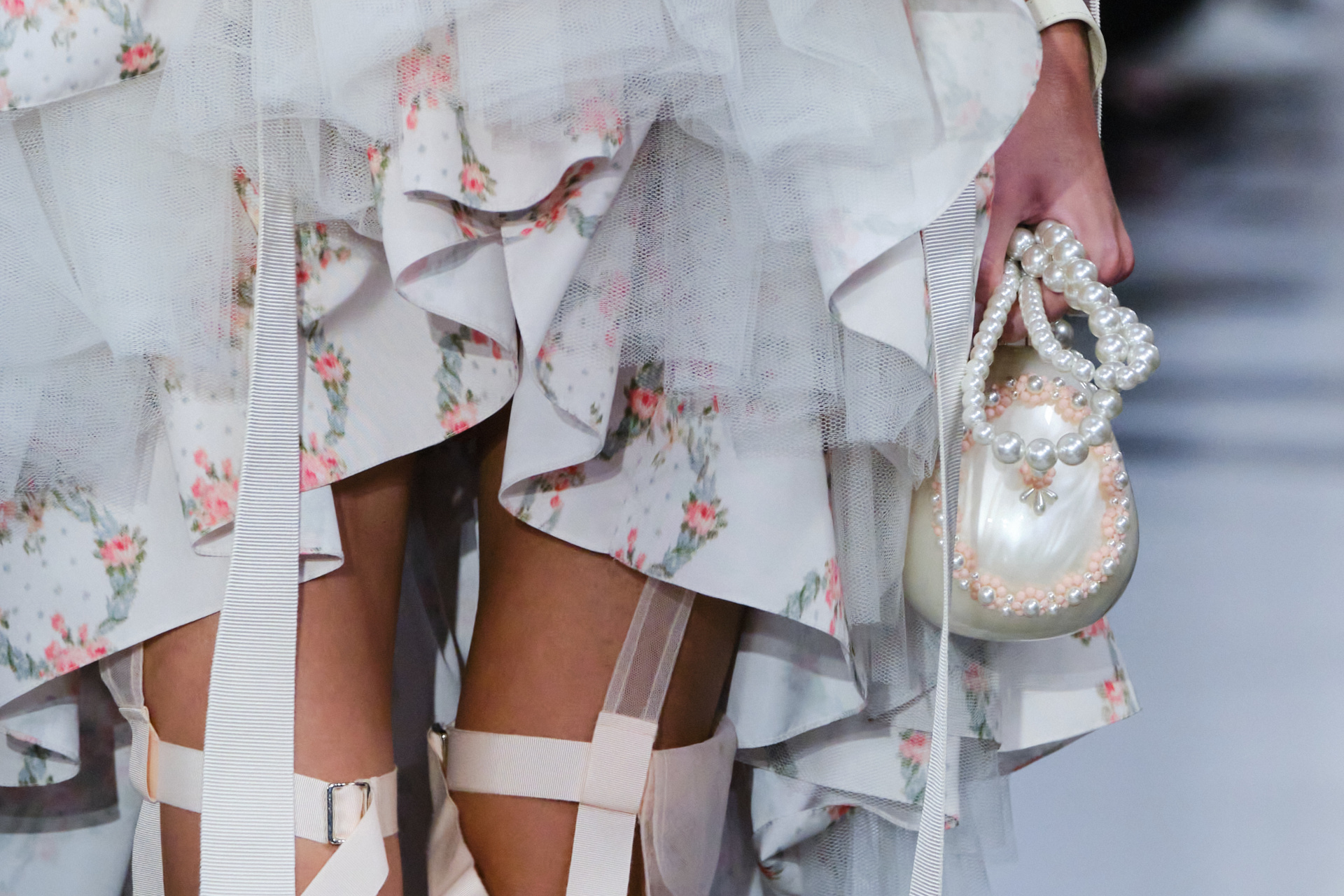 Close up of dress hemline and hand holding a pearl bag