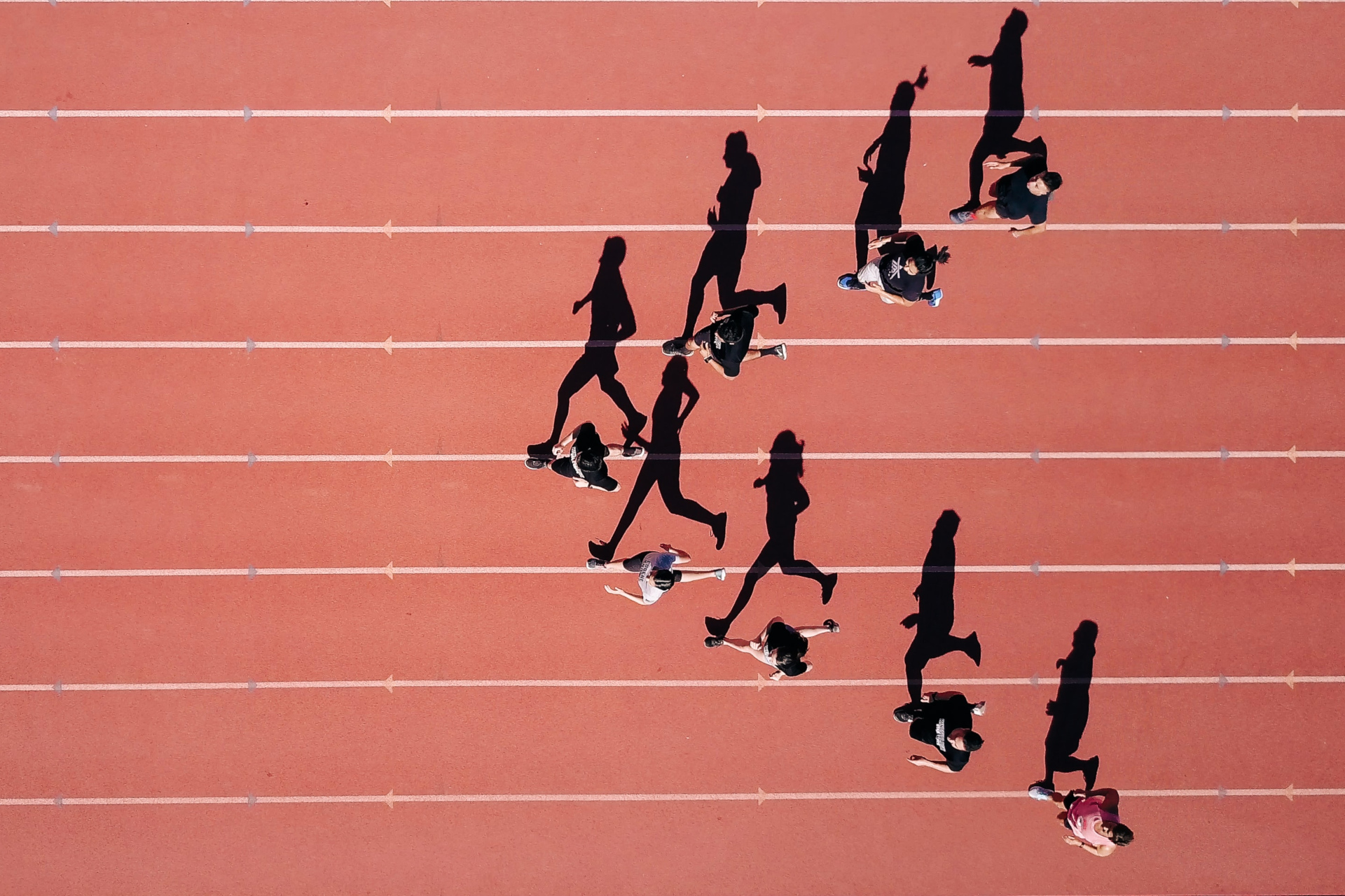 Overhead view of people running on red racetrack