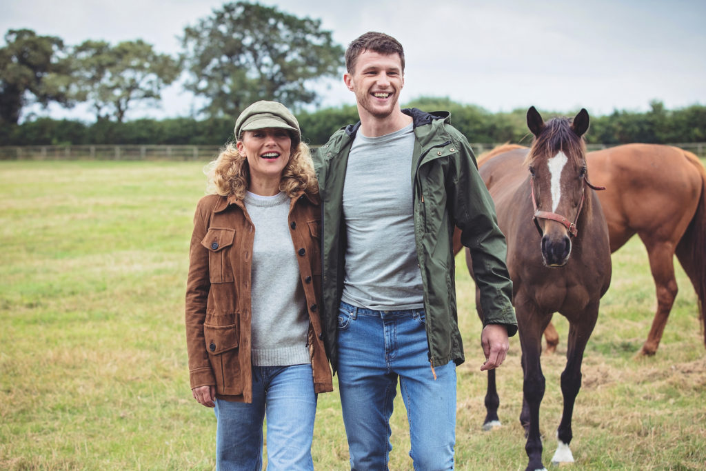 Male and female models in field with horses wearing Troy London clothes