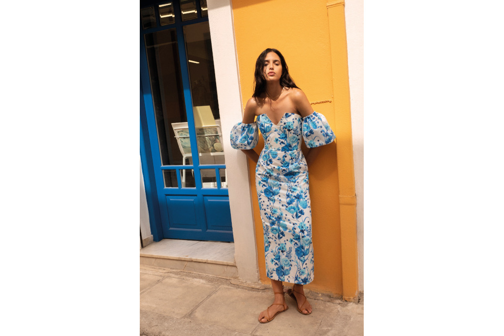 Woman in floral blue dress leaning against yellow wall