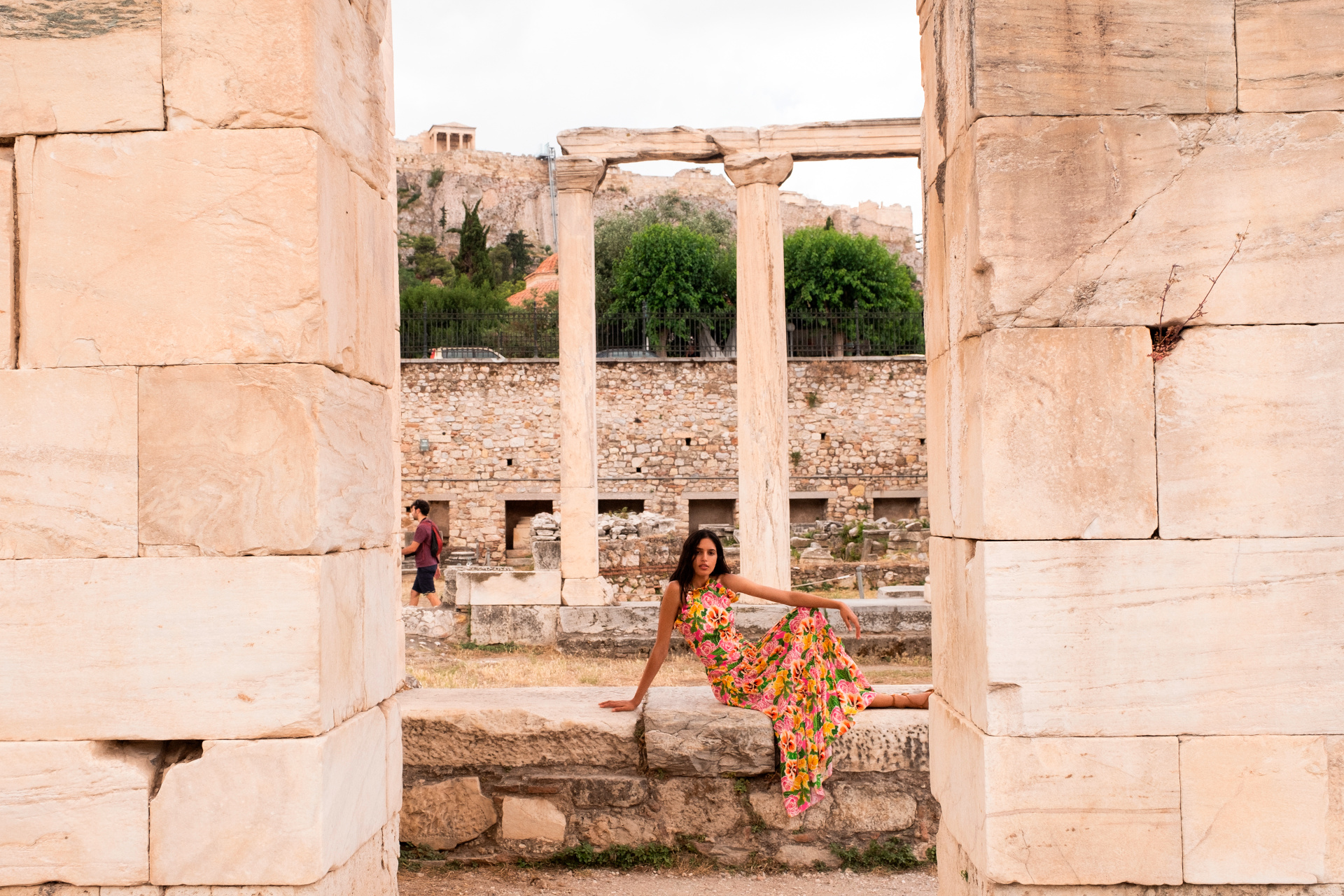 Woman in print dress sat on stone wall in old ruins