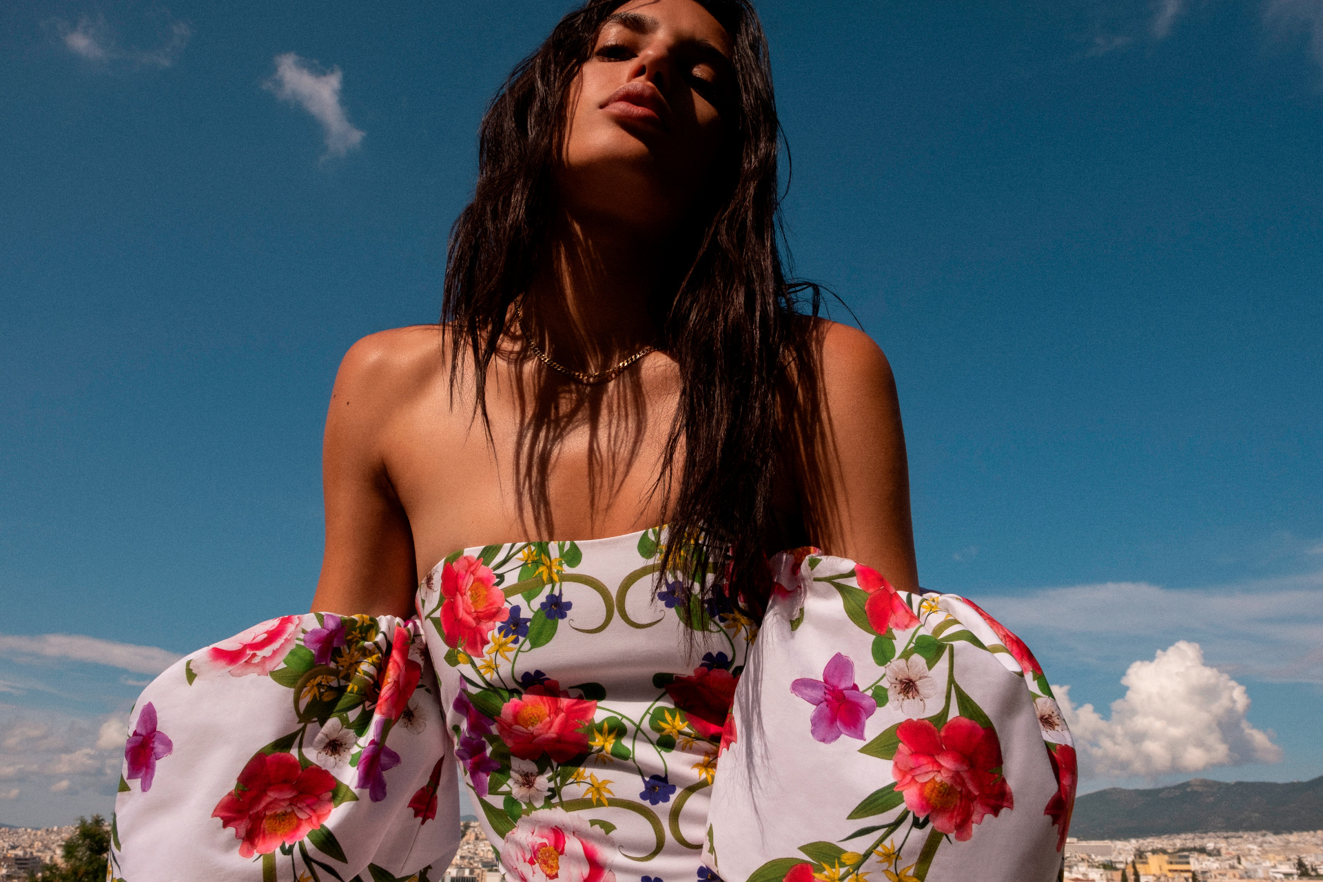 Close up of woman in floral print top and puff sleeves, stood in front of blue sky