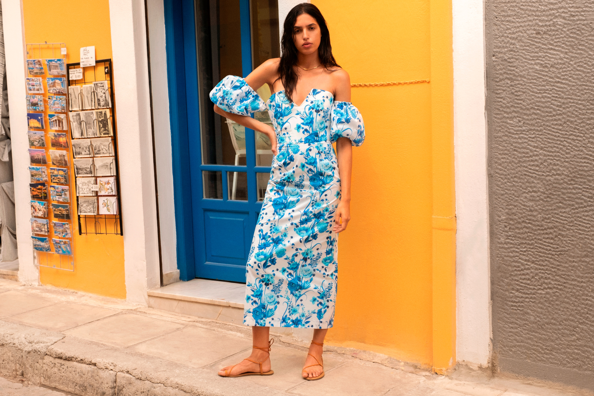 Woman in bvlue floral dress and puff sleeves stood in front of yellow and blue building