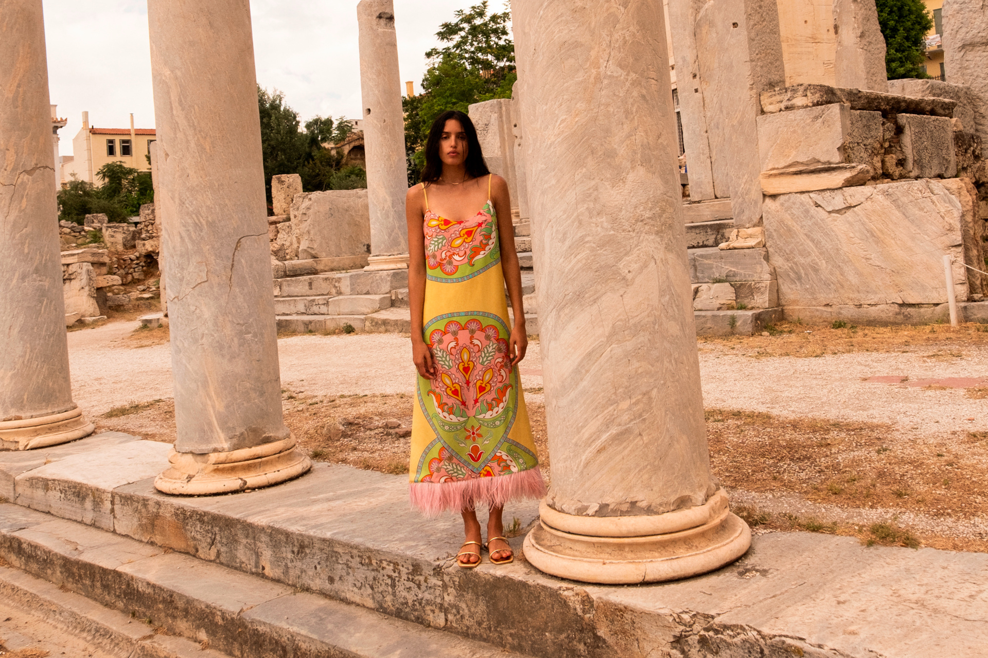 Woman in yellow patterned dress stood among stone columns