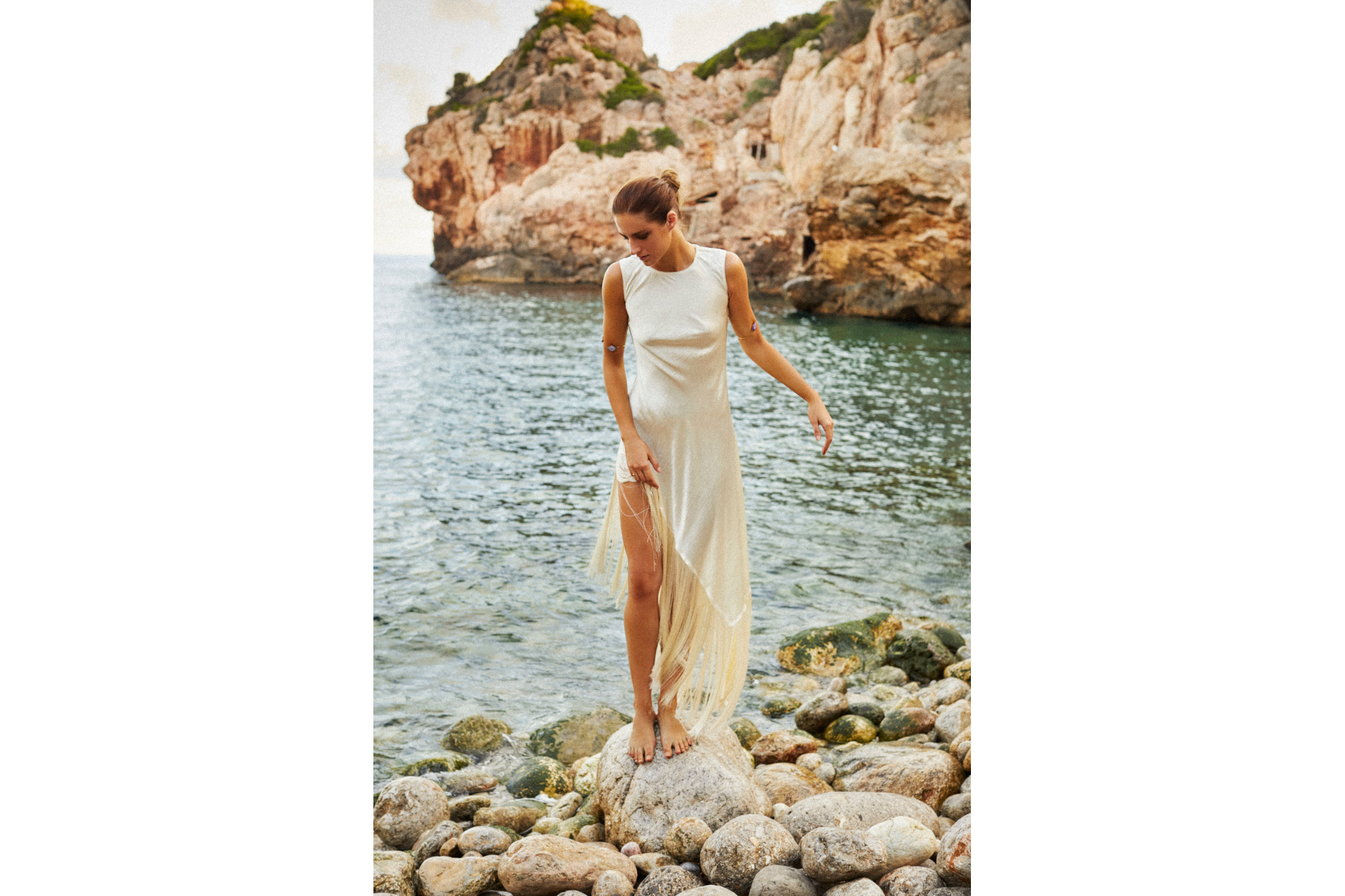 Woman in white dress on rocks by open water