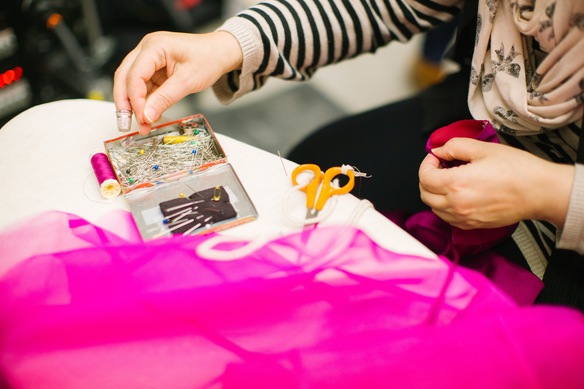 Close up of person in stripe shirt with a sewing kit sat next to pink tulle fabric